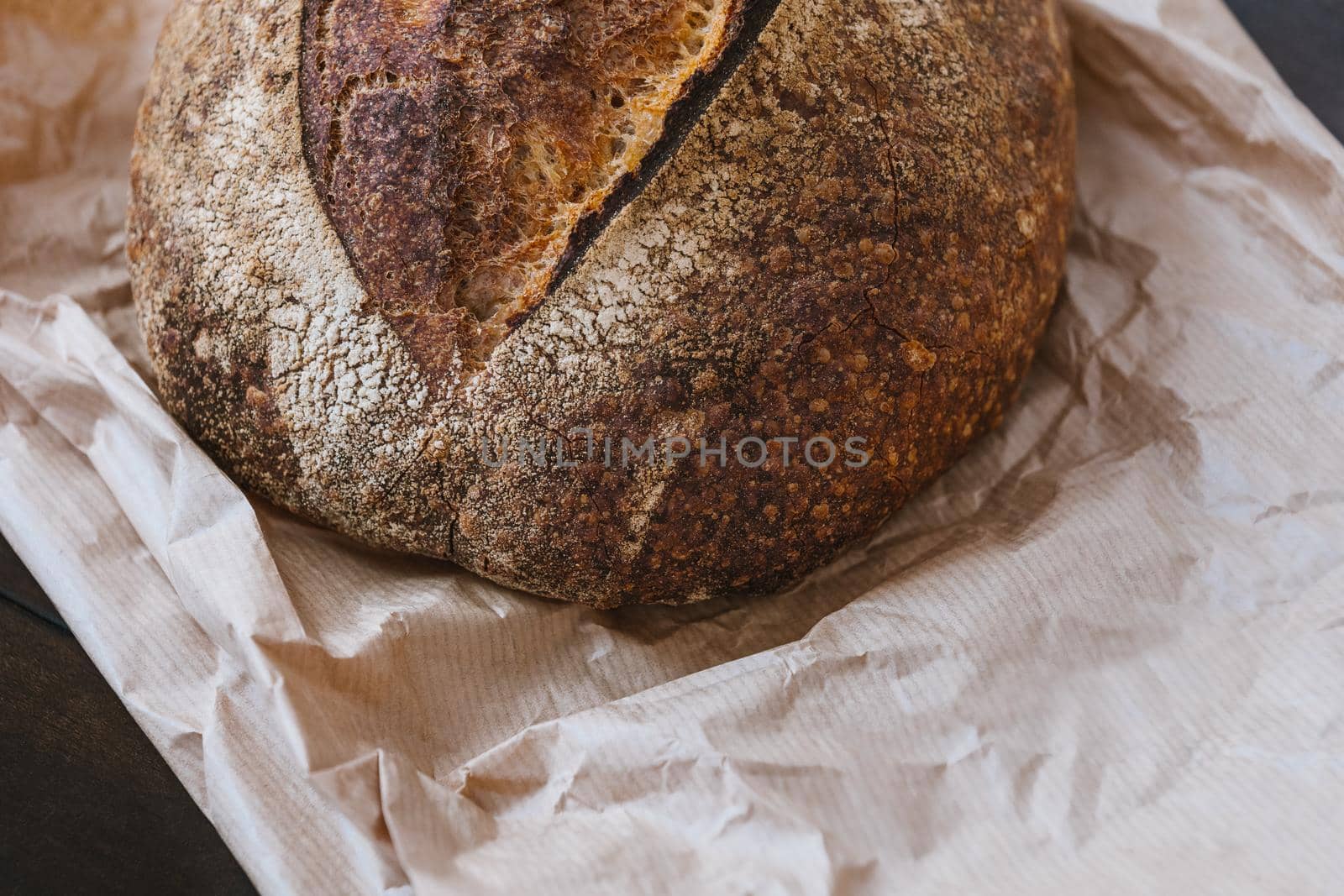 Homemade bread on craft paper on kitchen table. Crispy baked wheat bread surface texture. Selective focus. by apavlin