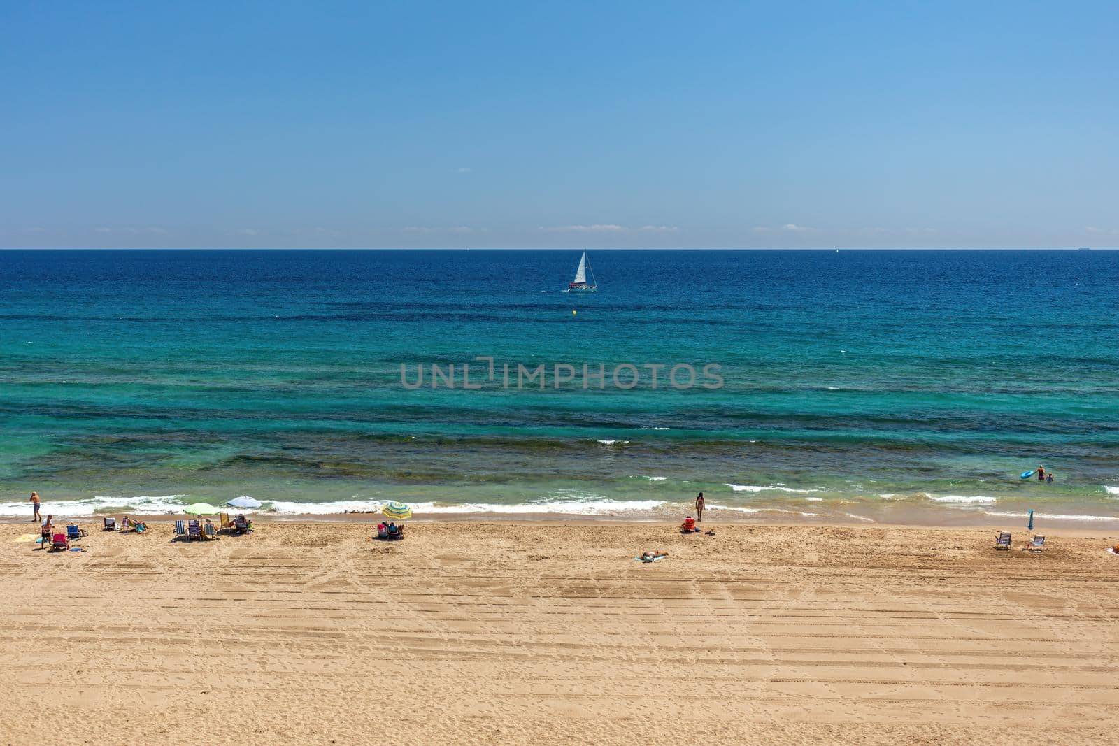 Beach with yellow sand, turquoise water and blue sunny sky. Tourists resting on the beach and looking to the mediteranian sea. by apavlin