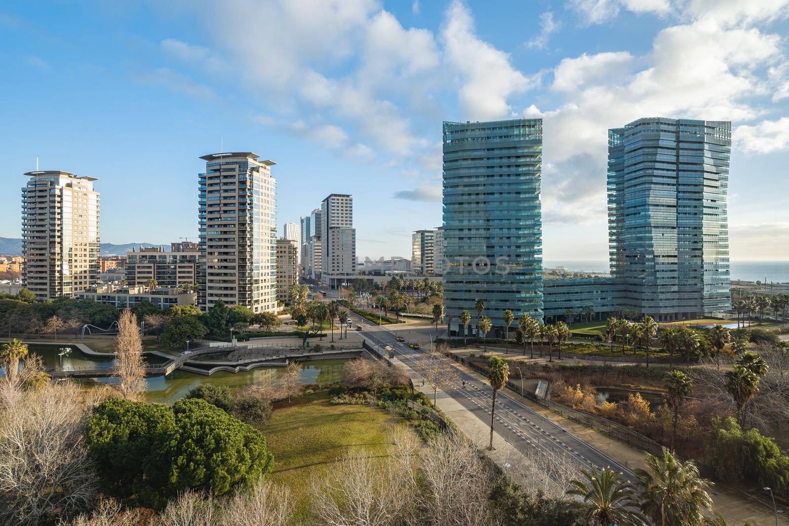 View of expensive area with park and modern high-rise buildings. Diagonal Mar district close to the sea in Barcelona, Spain. Sunny day with clouds.