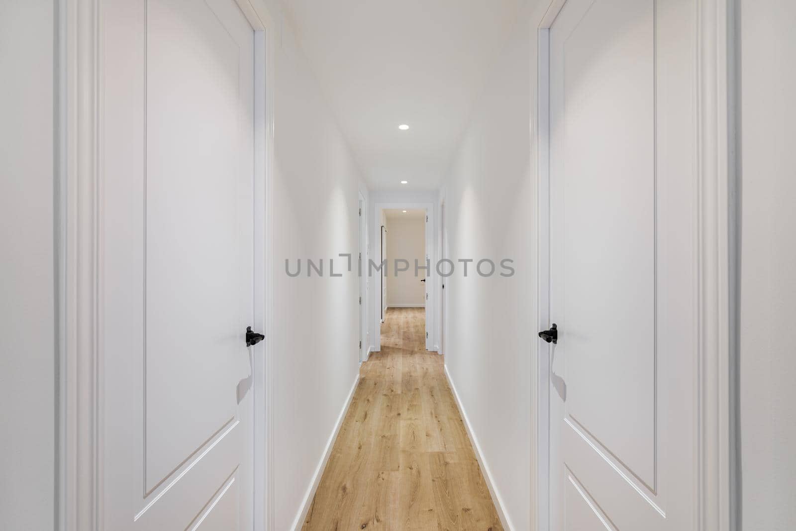 Interior of long narrow hallway with closed doors, wooden floor and white walls in apartment designed in minimal style by apavlin