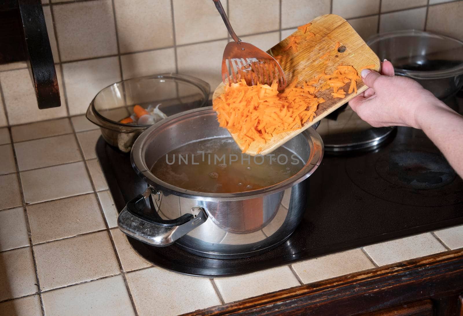 a woman puts grated carrots in a pan in the kitchen against the background of fresh vegetables, ingredients for step by step cooking soup. High quality photo