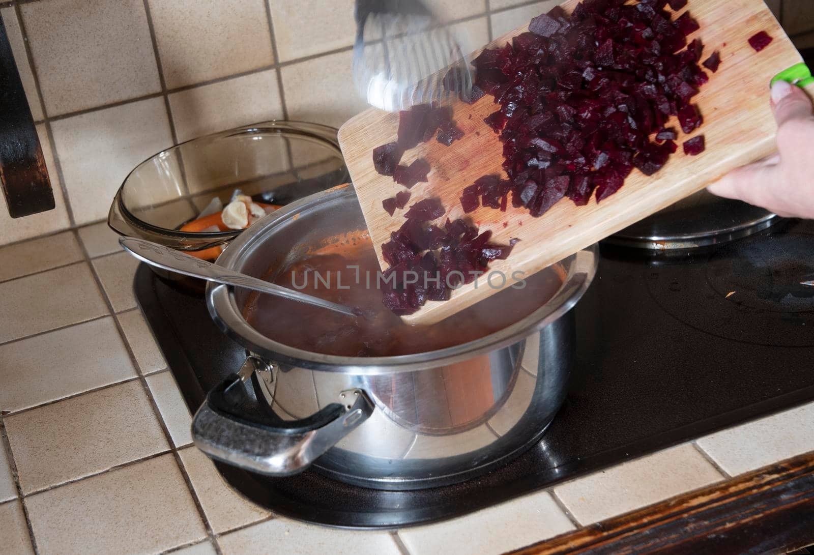 a woman puts a beetroot in a pot in the kitchen against the background of fresh vegetables, ingredients for step by step cooking soup. High quality photo