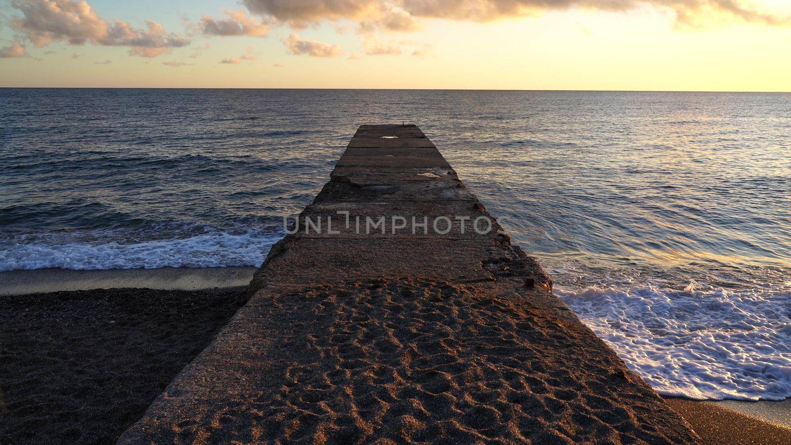 Old concrete pier on the seashore at sunset. Light wind and ripples on the sea. The concept of calm and serenity. Summer nature background, beautiful seascape, 4K