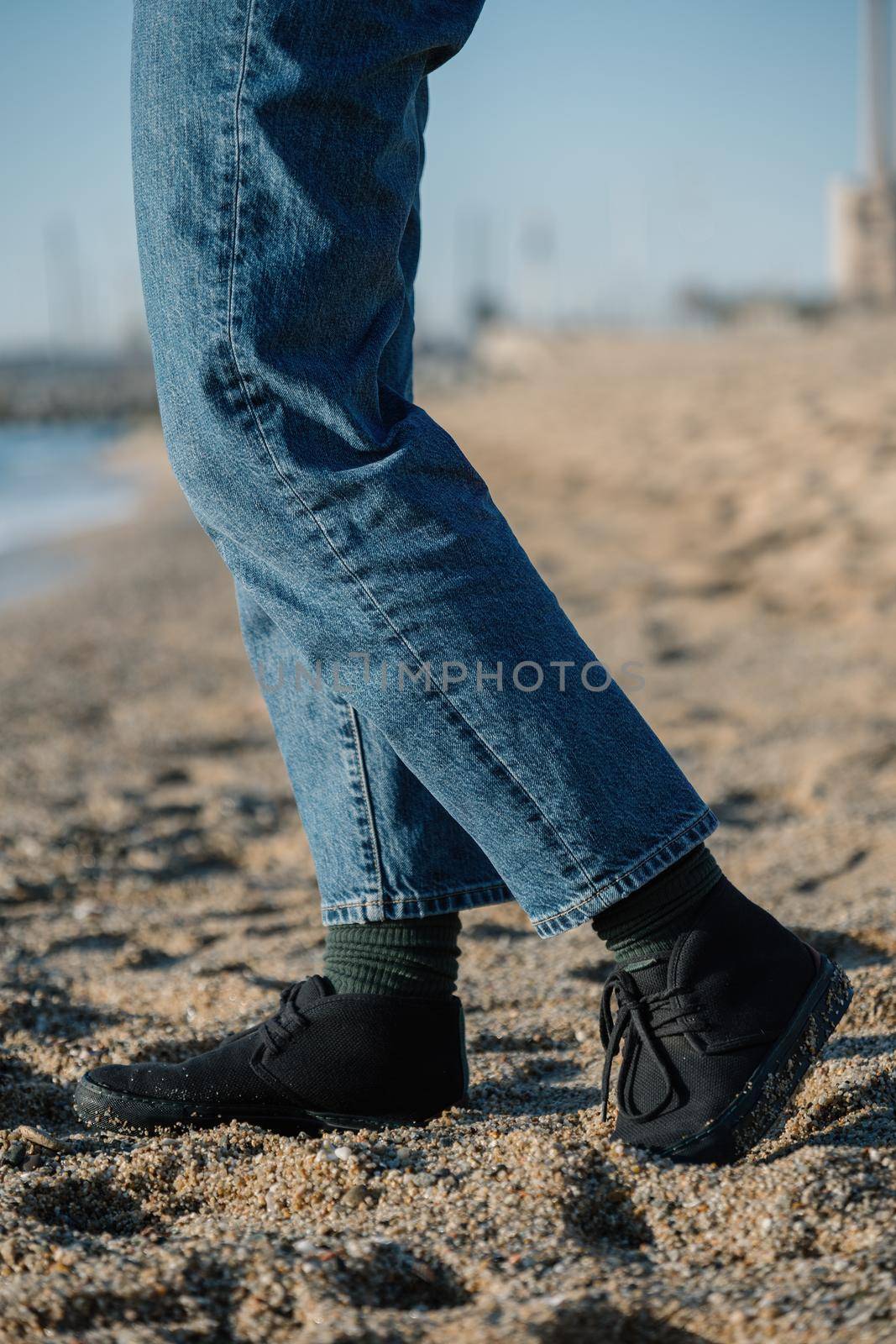 Legs of man in jeans and green socks on sand at a beach. Walking in comfortable shoes on beach