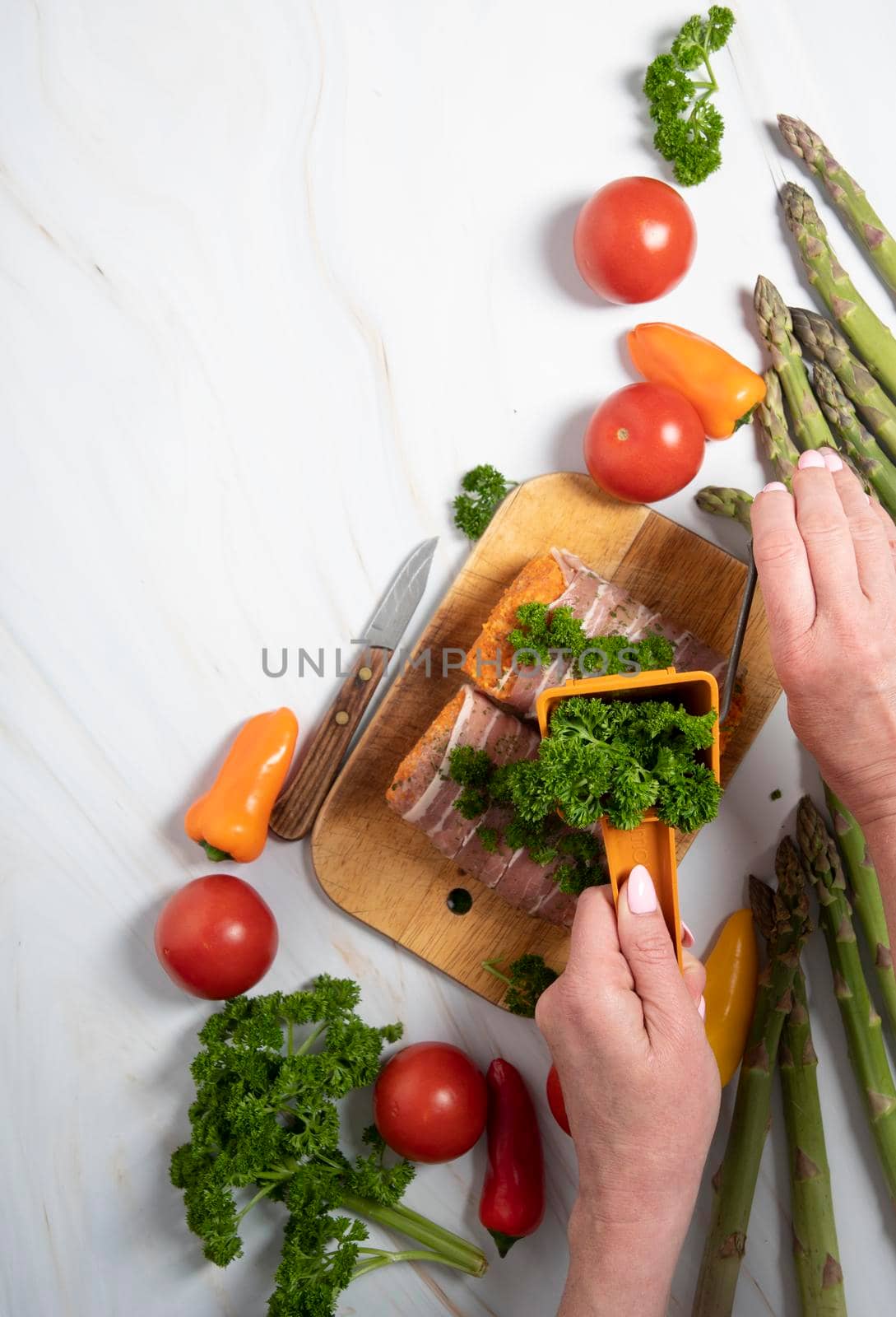 female hands decorate with parsley minced meat sausages in bacon with fresh vegetables, cherry tomatoes, sweet peppers, colorful food flat lay. High quality photo