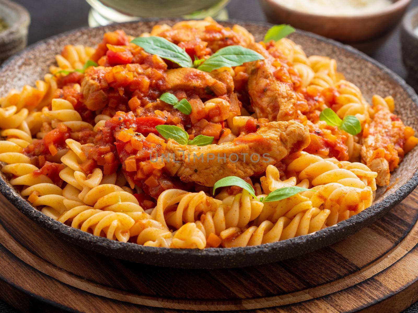 fusilli pasta with tomato sauce, chicken fillet with basil leaves on dark brown background, side view.