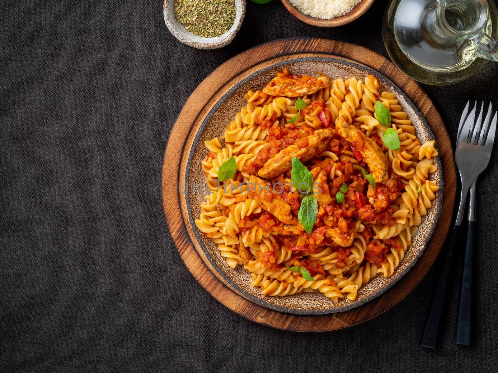 fusilli pasta with tomato sauce, chicken fillet with basil leaves on dark brown background, top view, copy space.