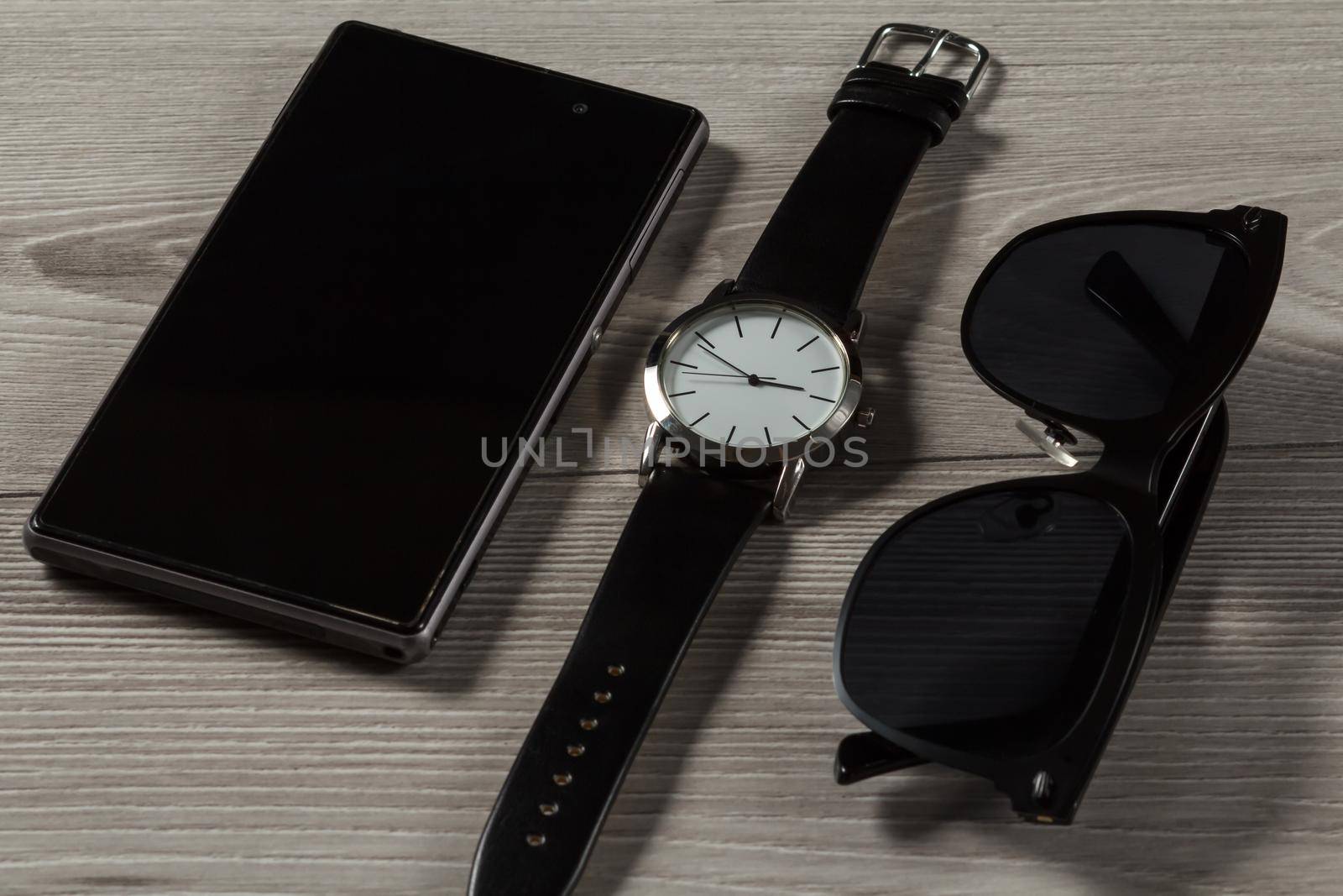 Watch with a leather strap, sell phone, black sunglasses on a gray wooden background