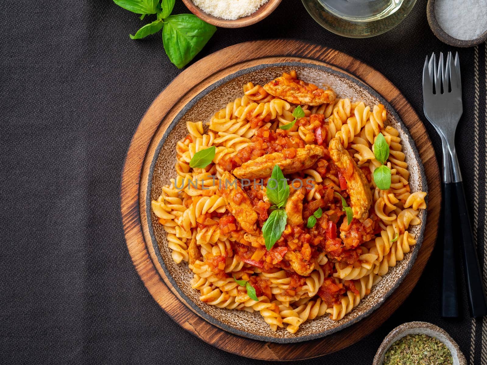 fusilli pasta with tomato sauce, chicken fillet with basil leaves on dark brown background, top view, copy space.