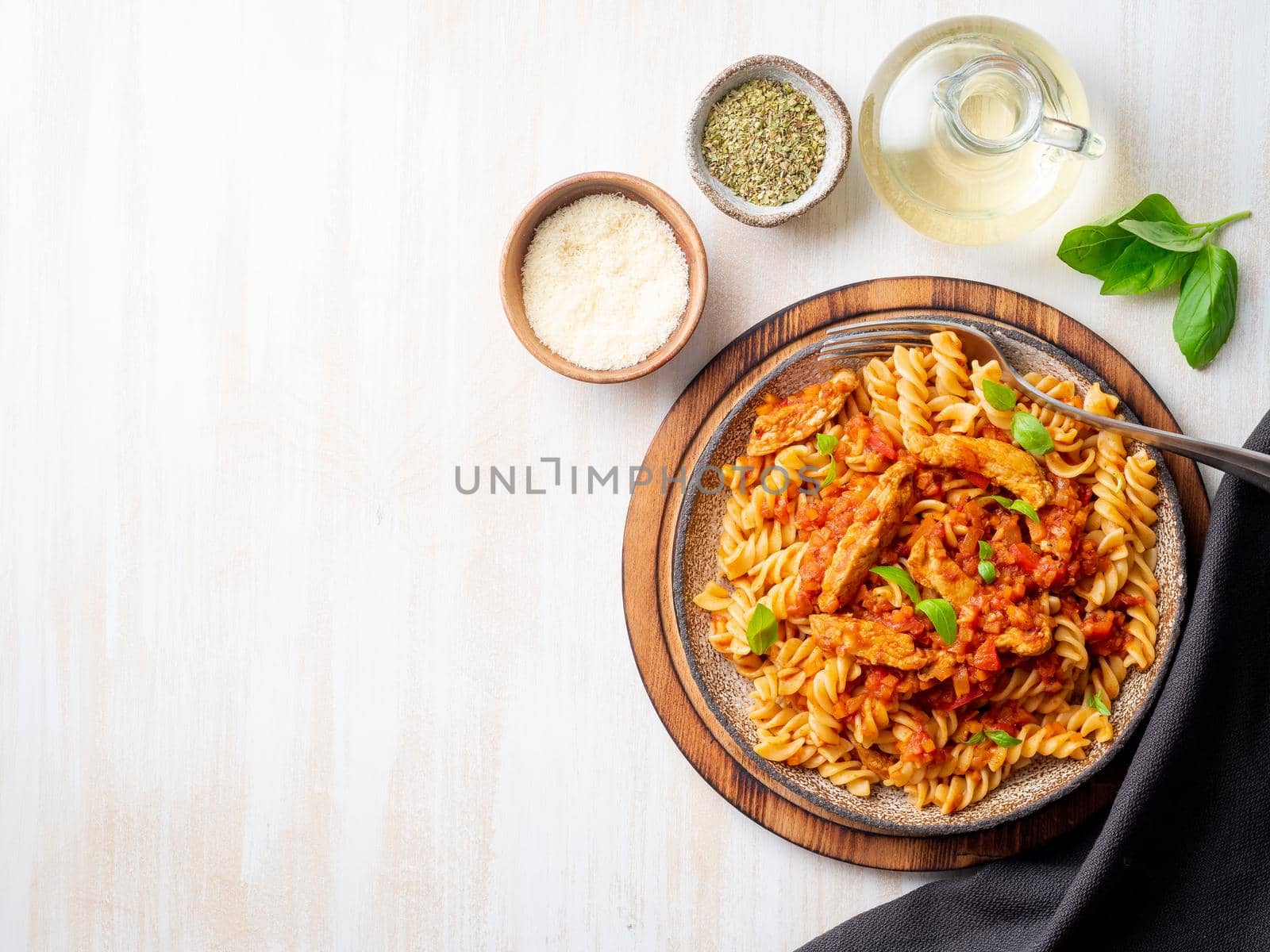 fusilli pasta with tomato sauce, chicken fillet with basil leaves on light white wooden background, top view, copy space.