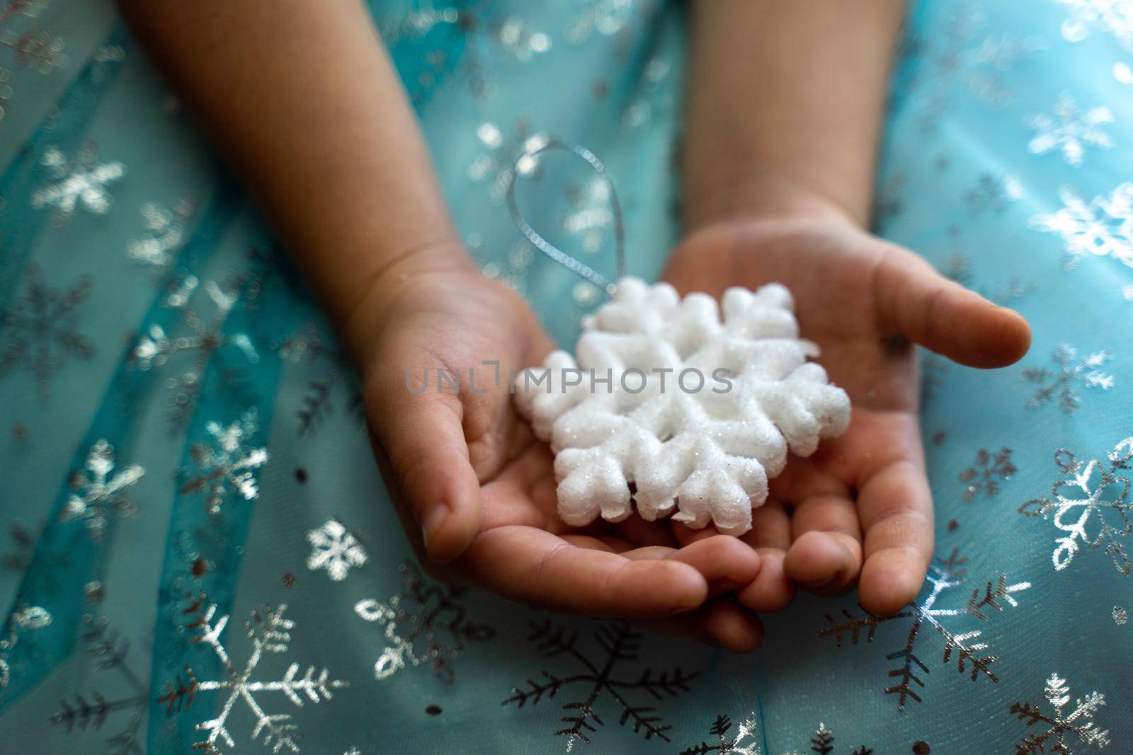 Winter and Christmas concept. Children's hands close-up holding a magic snowflake on the background of a blue dress with snowflakes.