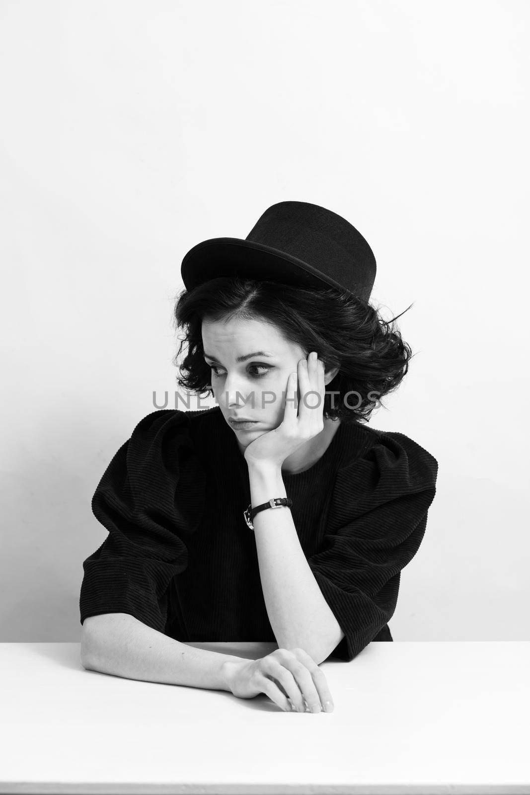 A woman in a hat sits at a table, white background. High quality photo
