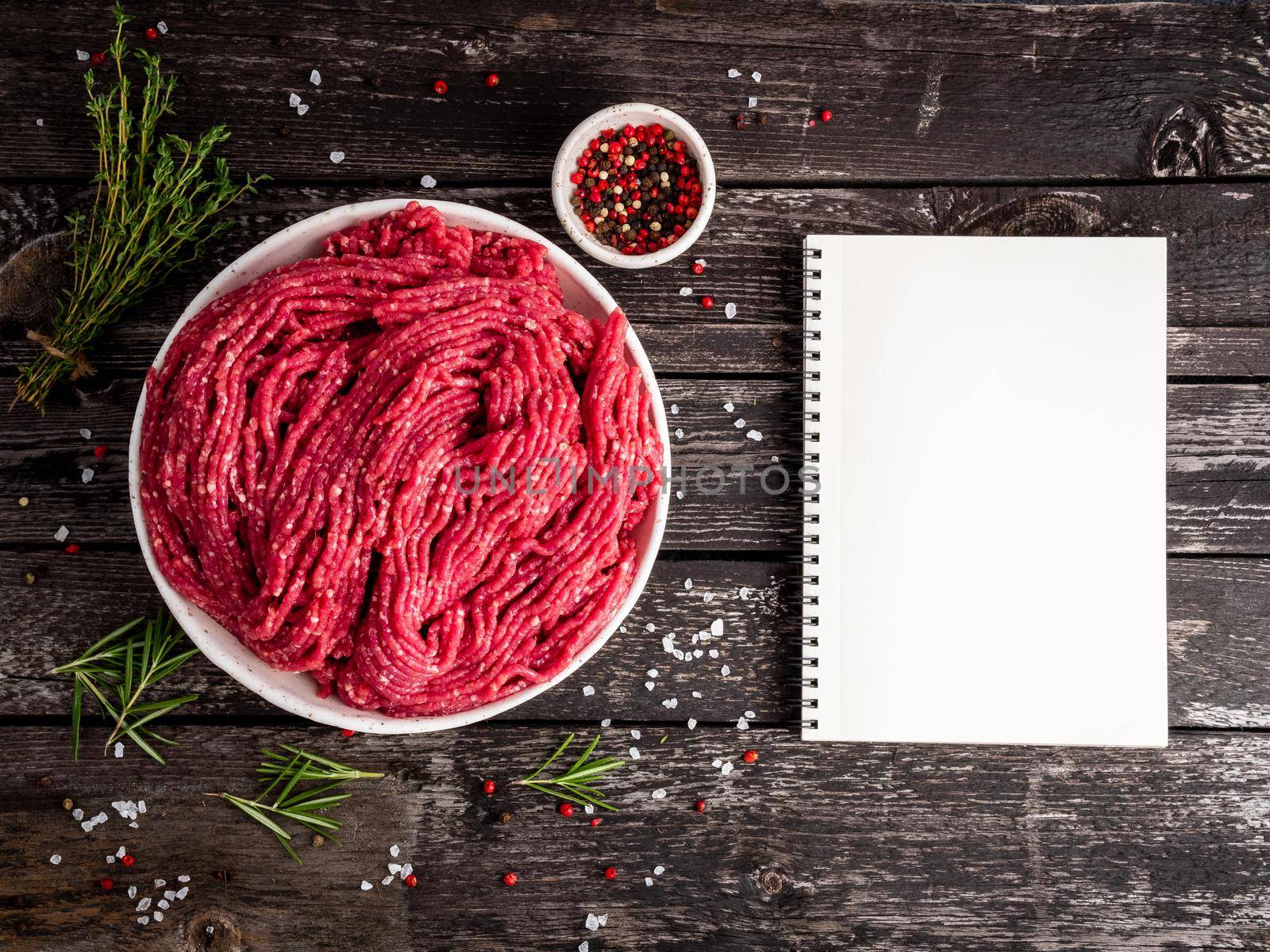 Mince beef, ground meat with ingredients for cooking on old gray dark wooden rustic table, notepad, recipe mock-up, top view, copy space.