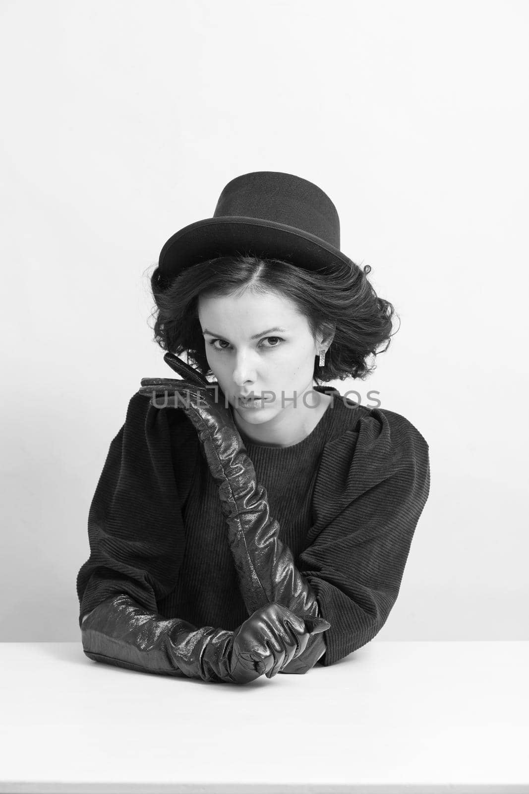curly woman in a hat and gloves sits at a white table, black and white photo. High quality photo
