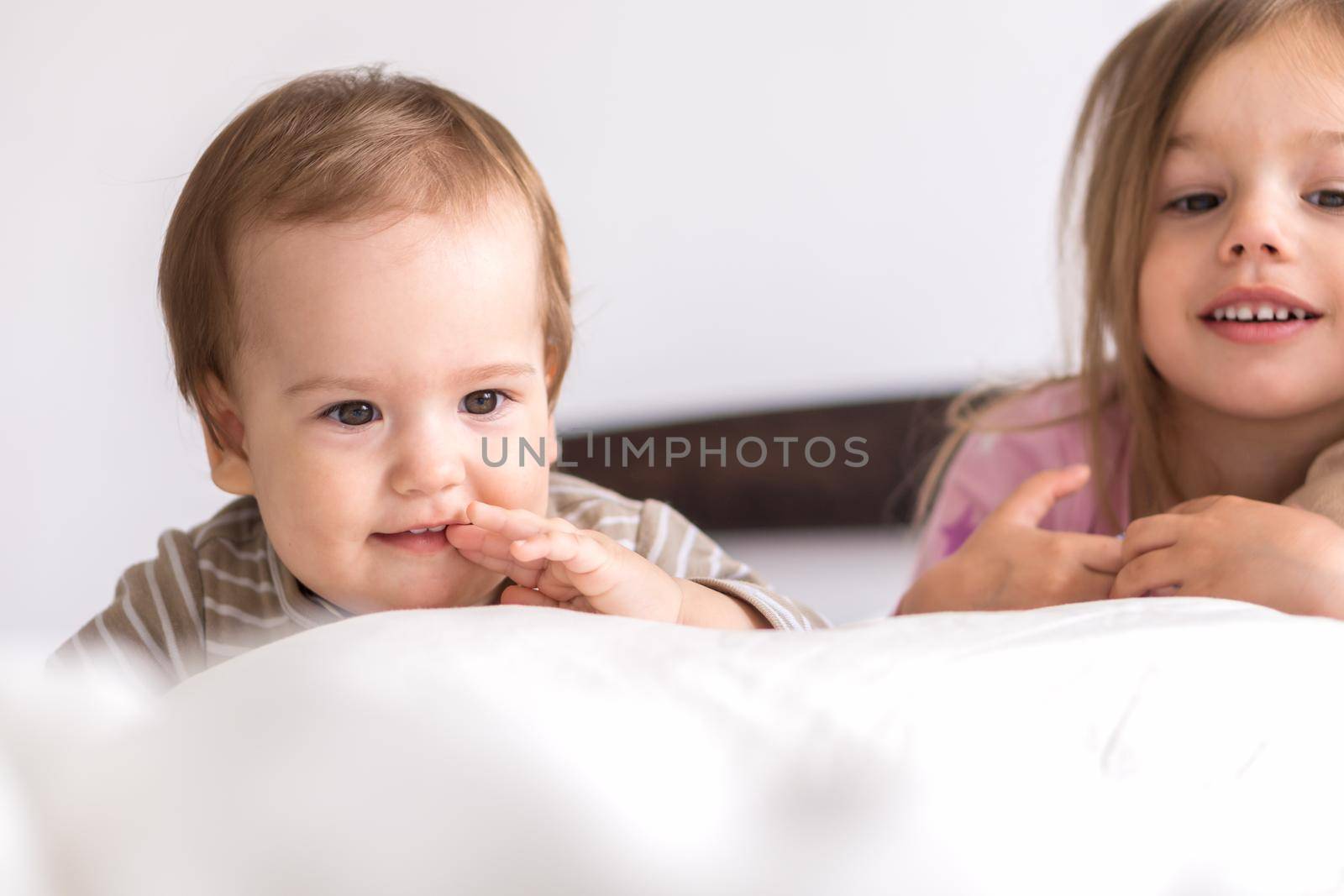 Little Preschool Toddler Minor Children Siblings Kids Watch Cartoon Use Smartphone Phone Device Together. Baby In Pajama On White Bed At Home Bedroom. Family, Leisure, Childhood, Friendship Concept.