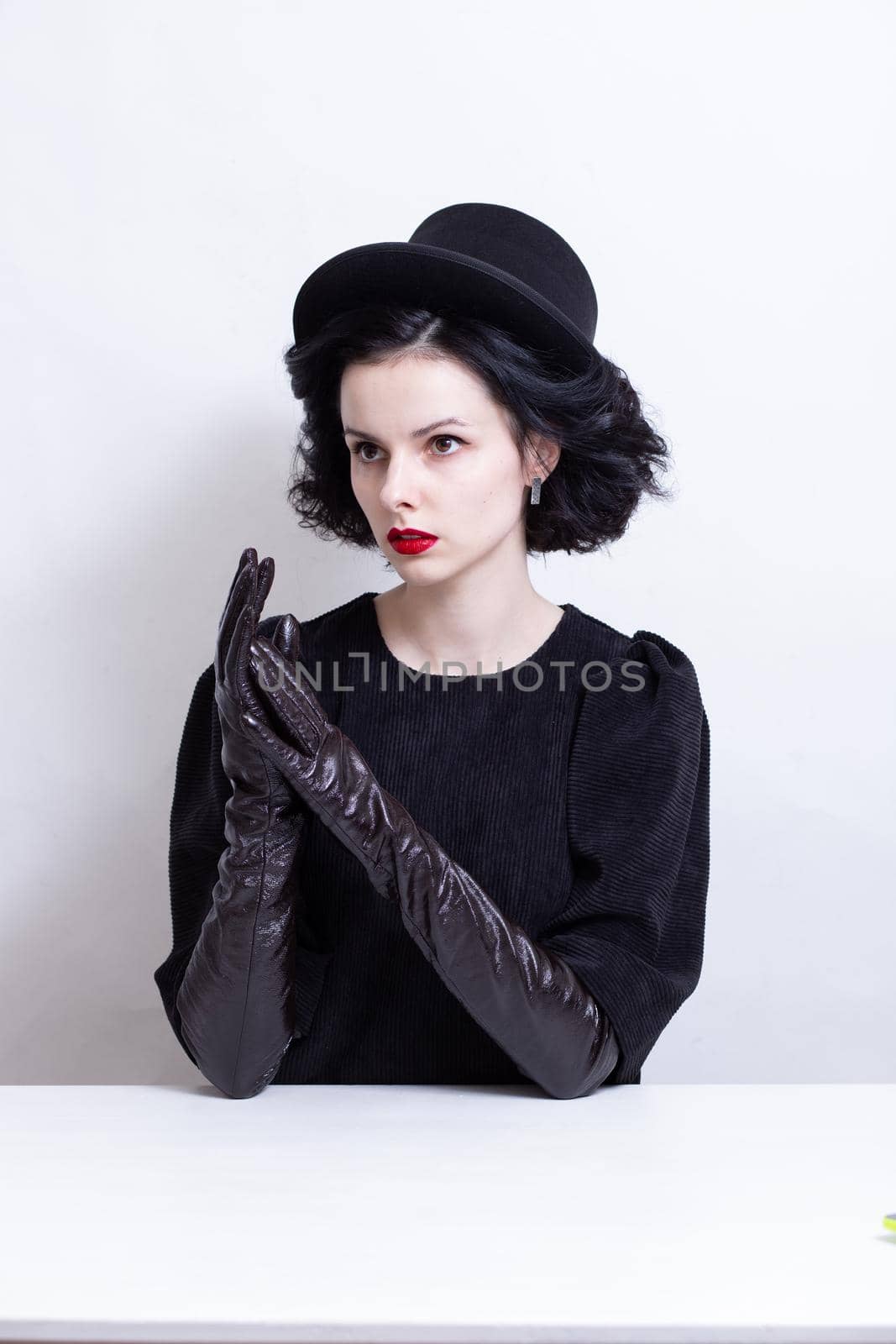 a woman with red lips, curly hair in a black hat and gloves sits at a table. High quality photo