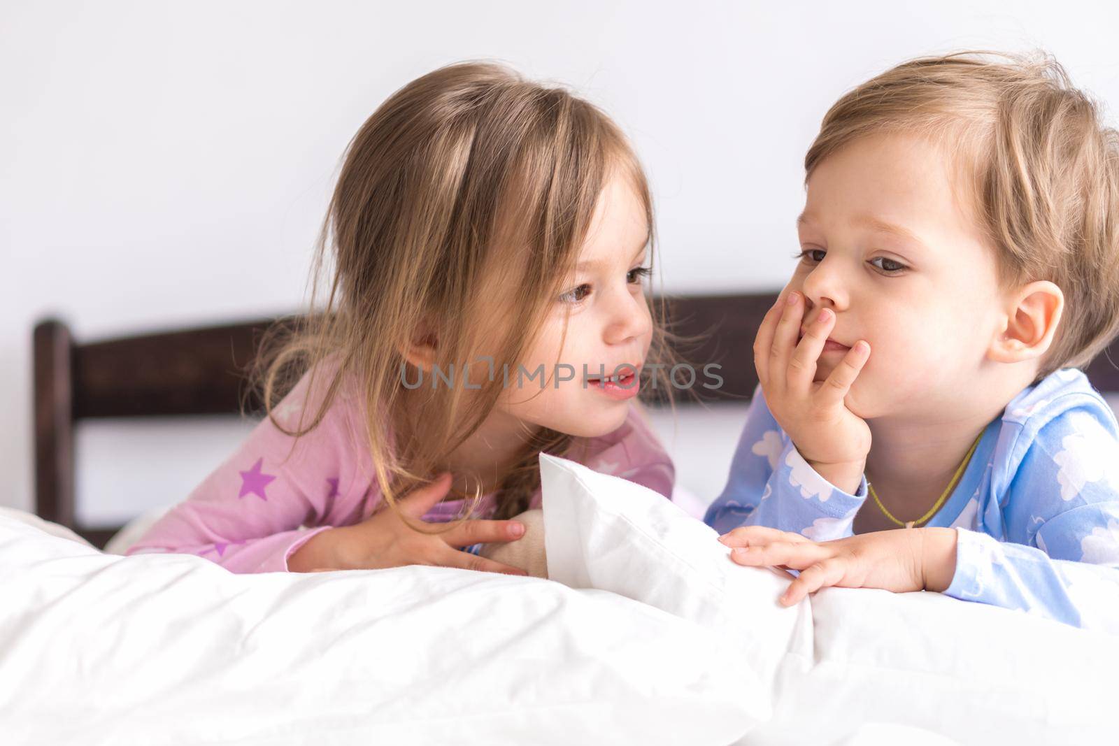 Little Preschool Toddler Minor Children Siblings Kids Watch Cartoon Use Smartphone Phone Device Together. Baby In Pajama On White Bed At Home Bedroom. Family, Leisure, Childhood, Friendship Concept.
