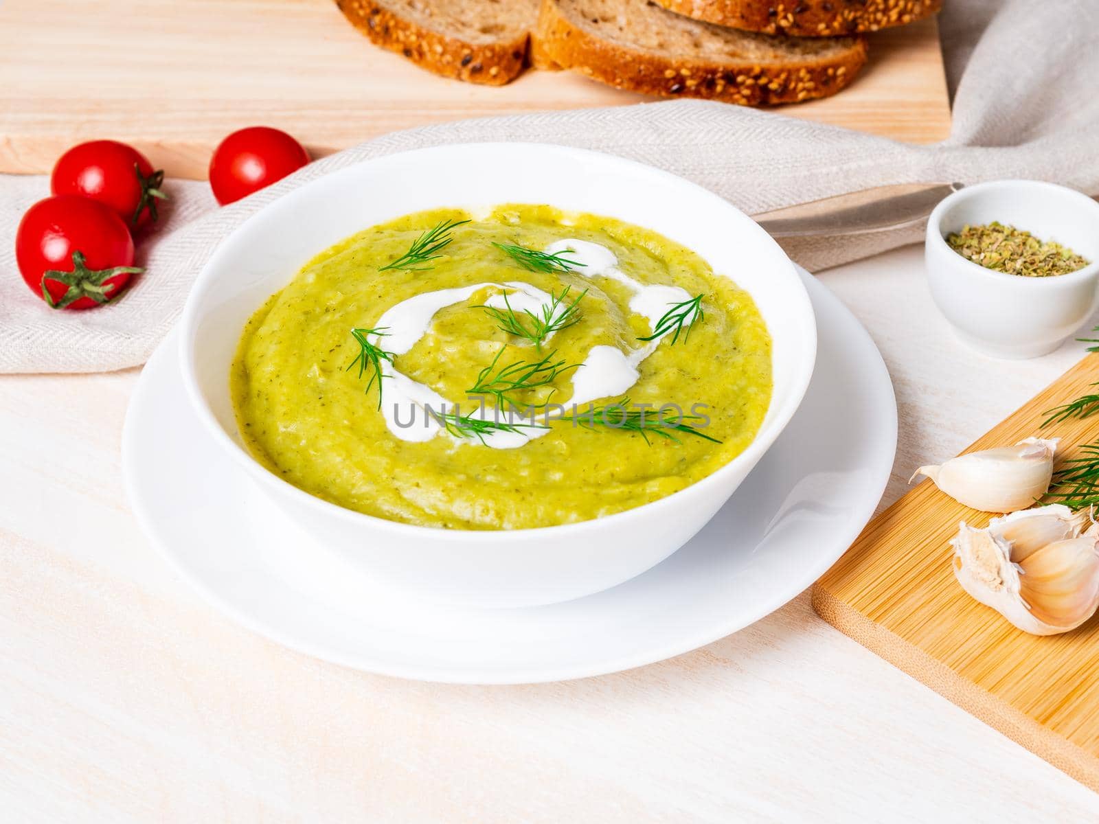 large white bowl with vegetable green cream soup of broccoli, zucchini, green peas on white background, side view.