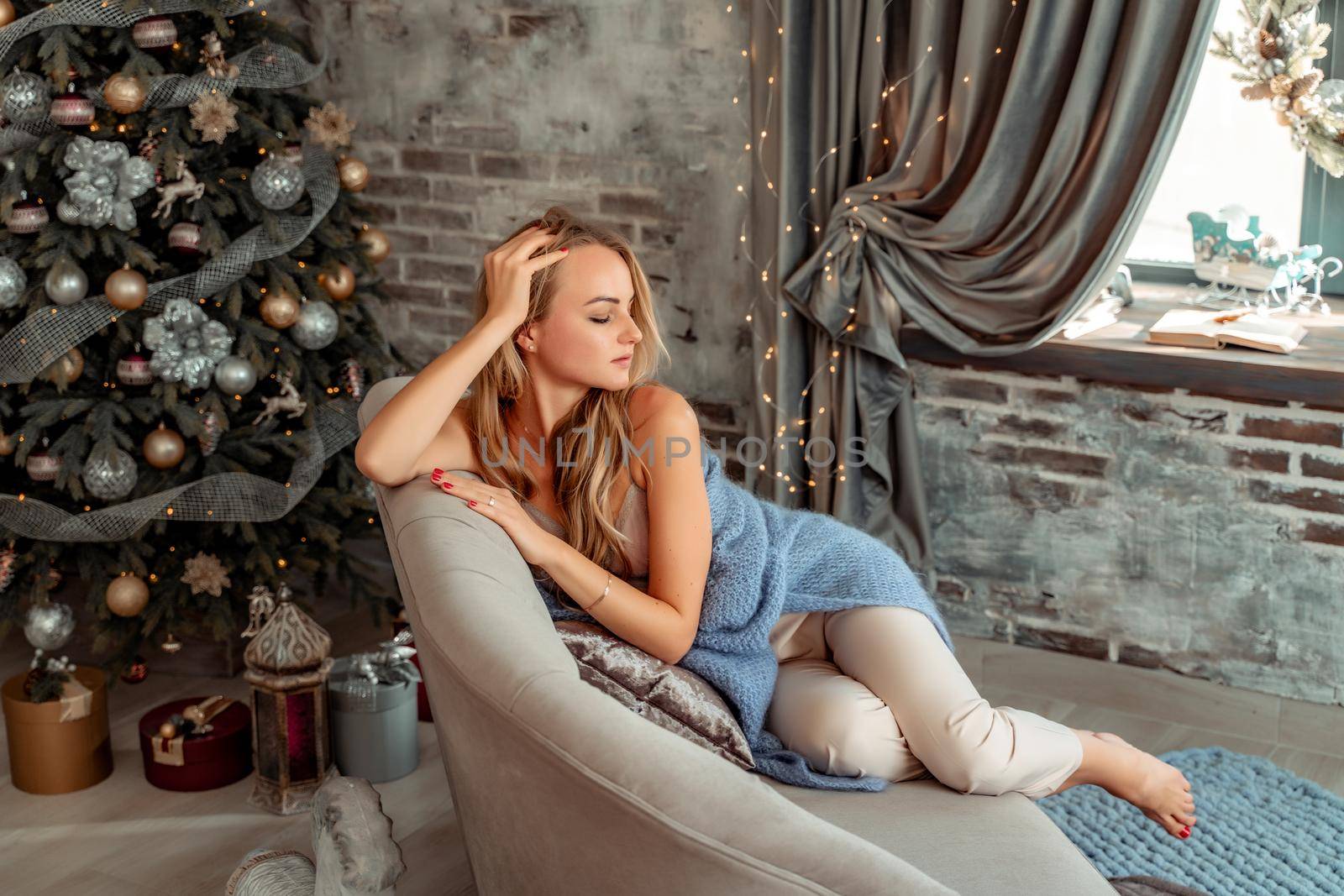 A young blonde woman is sitting on the sofa. The room is decorated with a Christmas tree