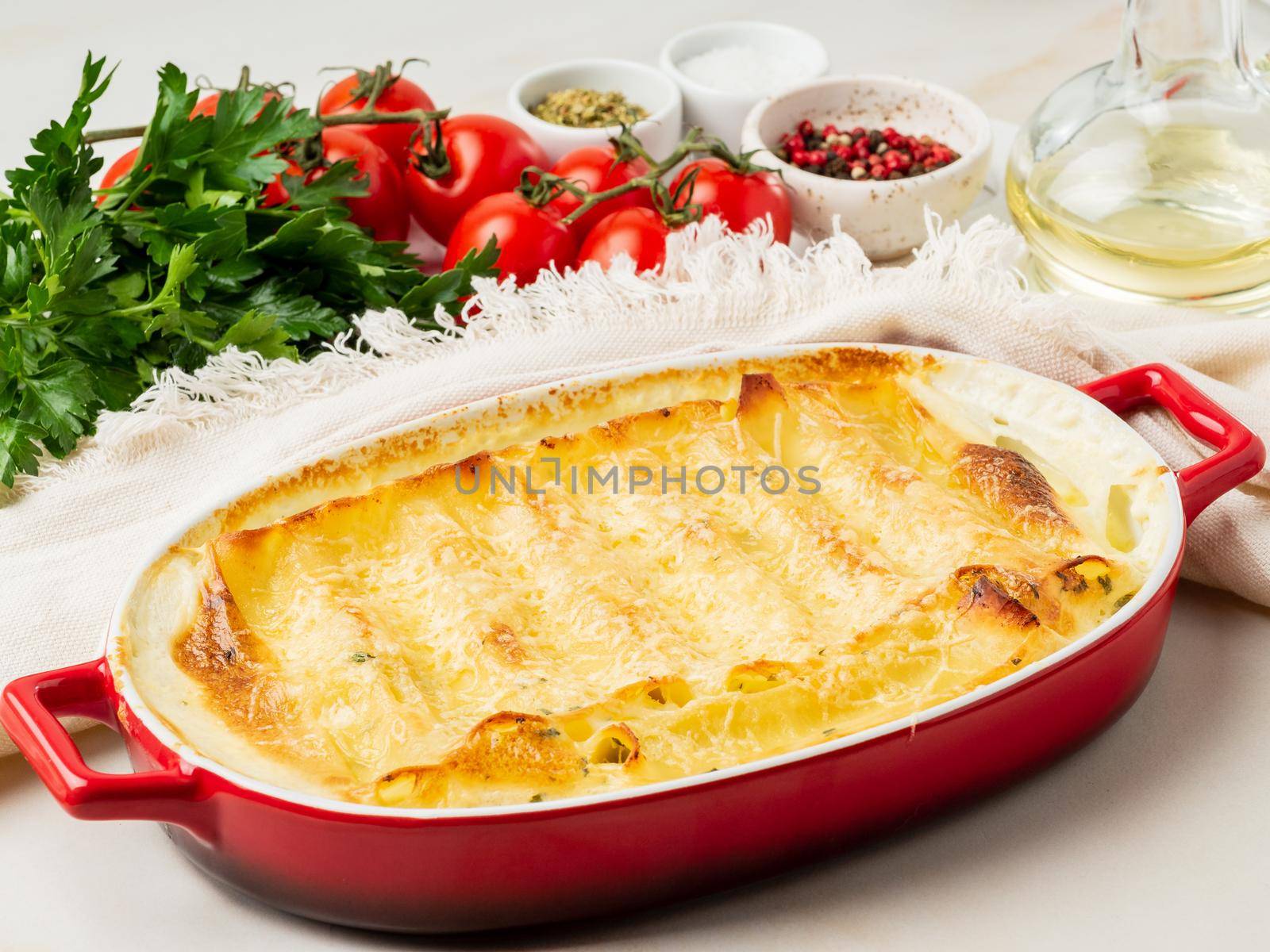 Cannelloni with filling of ricotta and parsley, baked with béchamel sauce, side view, white marble background