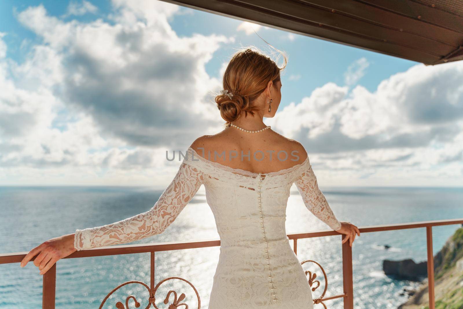 Beautiful Bride in wedding dress, outdoor portrait. Brunette elegant woman in luxurious fashion white gown enjoying on balcony. Attractive girl with long blowing hair style. by Matiunina