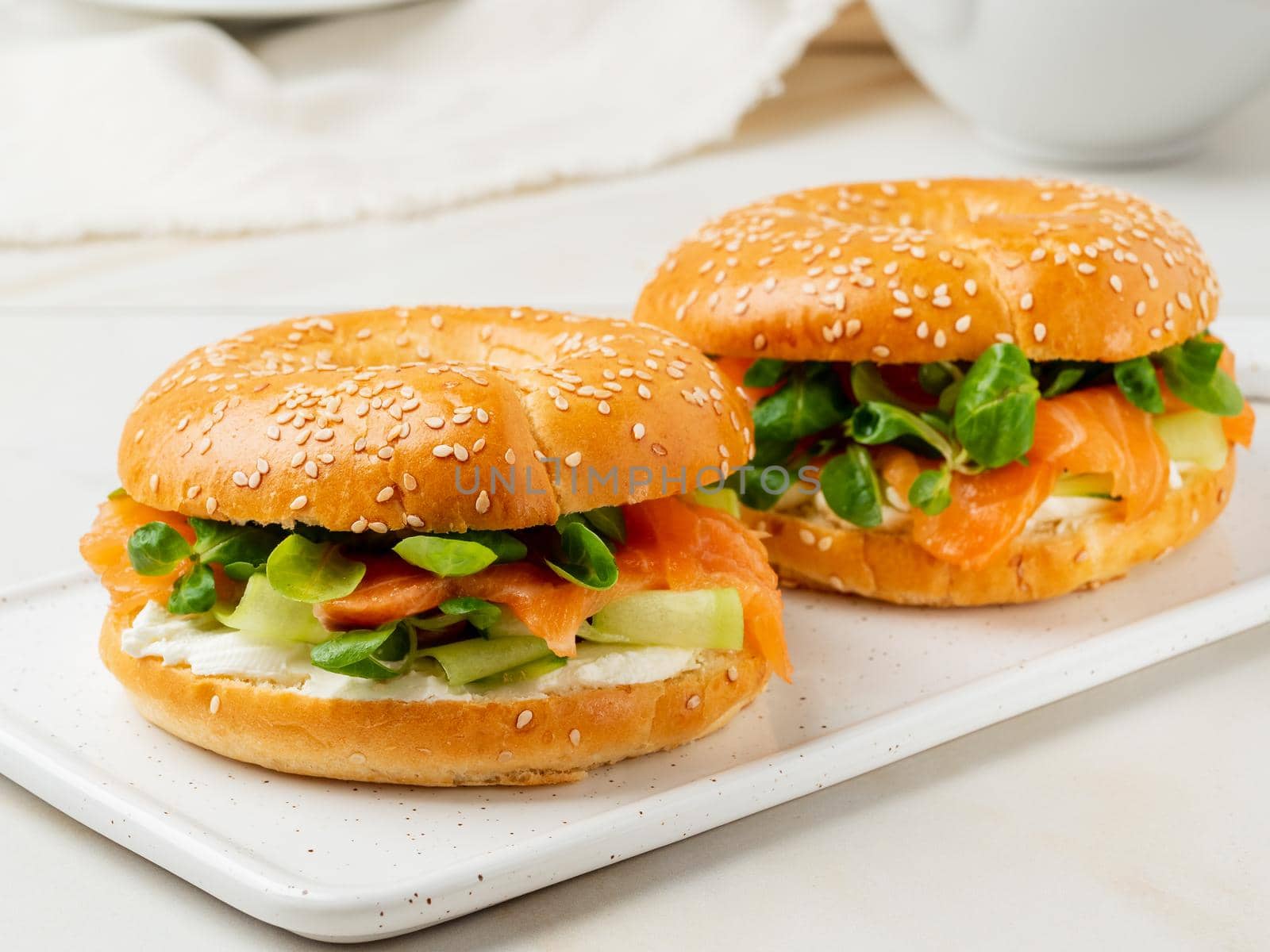 Two sandwiches with salmon, cream cheese, cucumber slices on white marble table