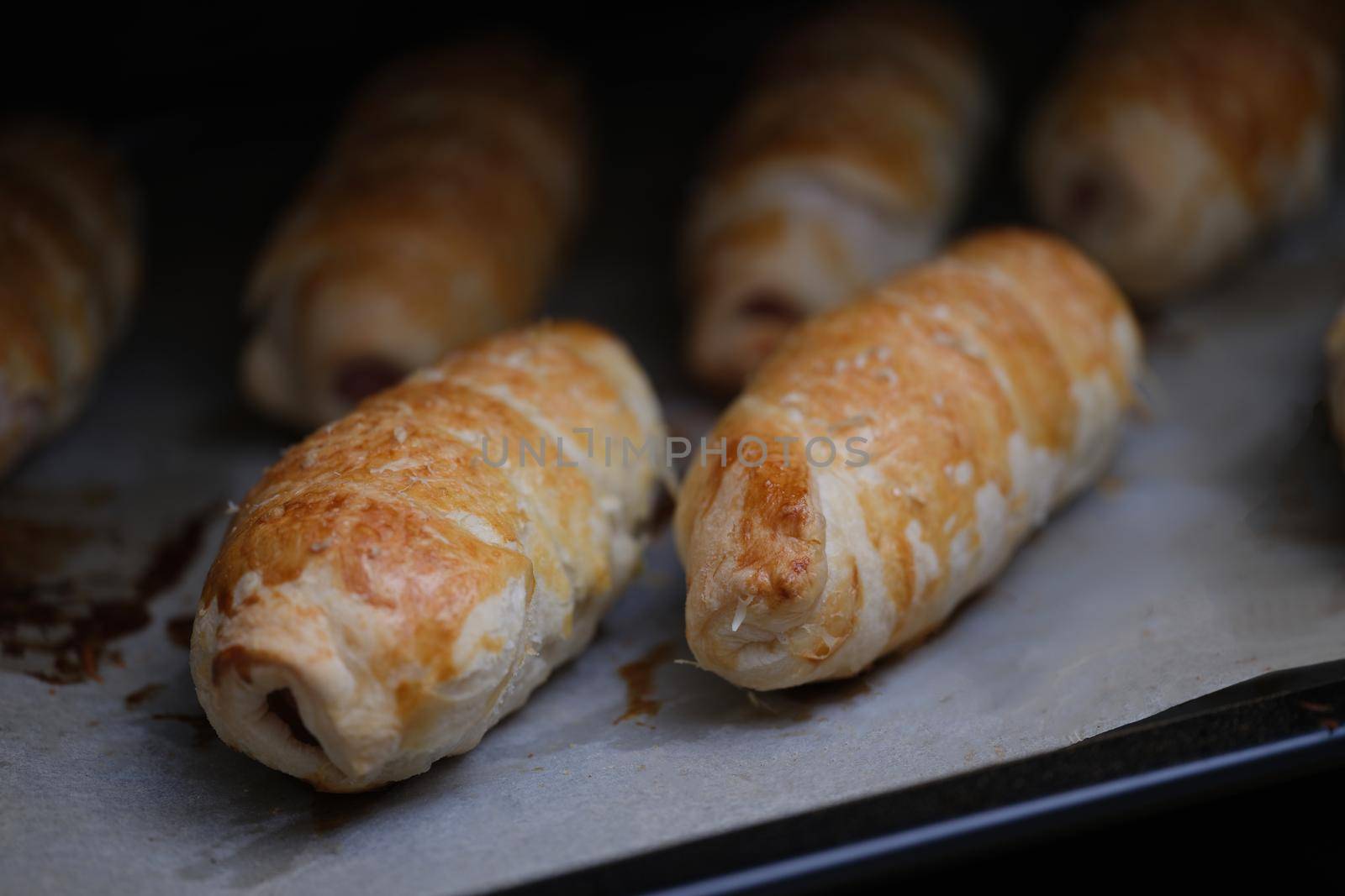 Close-up of homemade sausages in dough on baking sheet. Freshly baked sausage rolls. Lunch and yummy snack concept