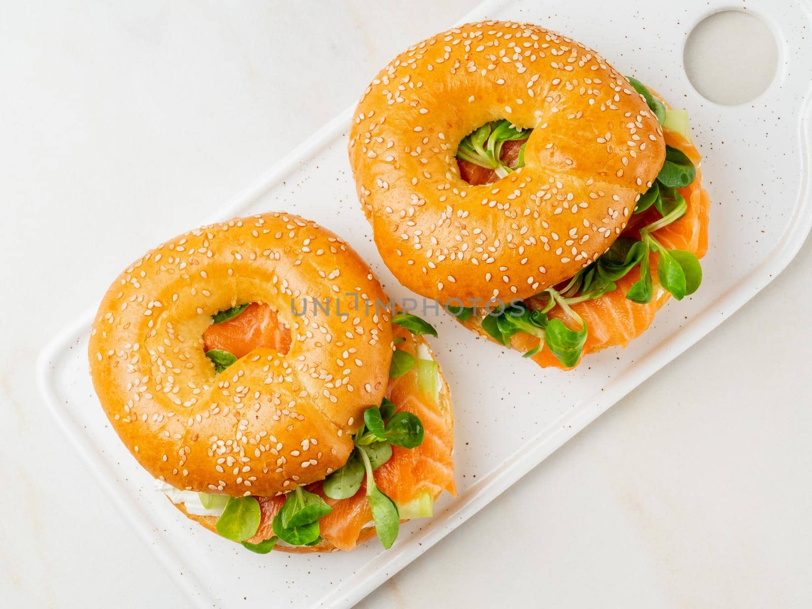 Two sandwiches with salmon, cream cheese, cucumber slices on white marble table