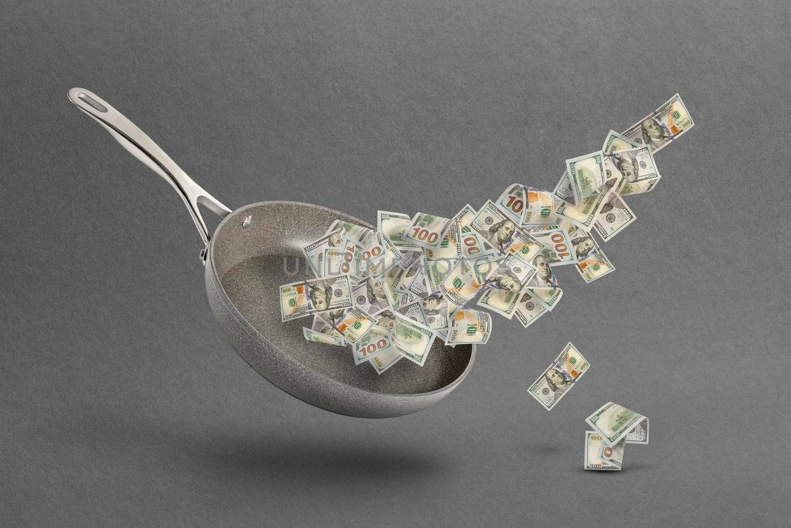 Rising food prices. The concept of rising cost of food. Money in a pot. Dollar bills fly over a frying pan as a symbol of money or salary for food on a gray background.