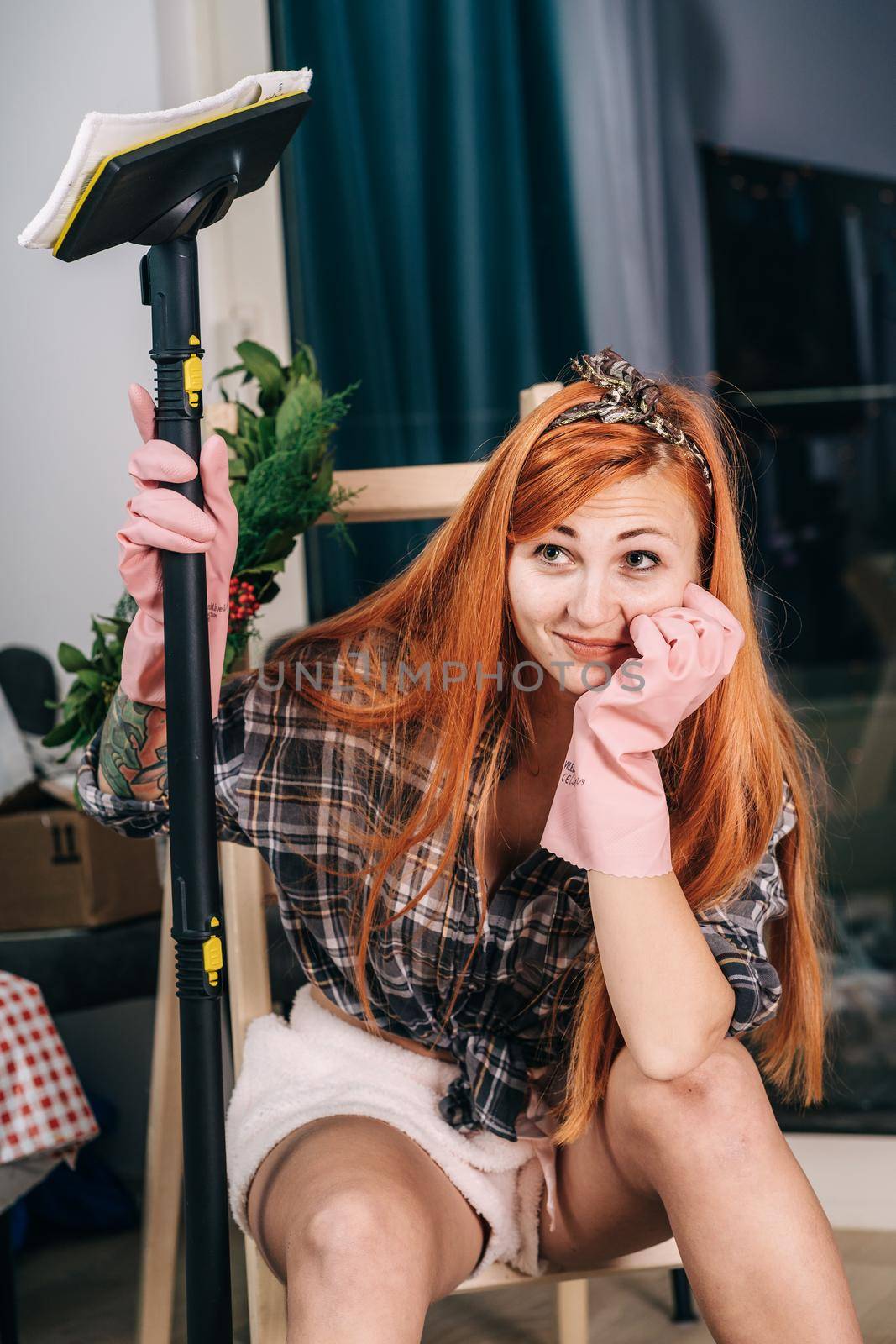 A housewife in rubber gloves holds a vacuum cleaner in her hands by Praximon