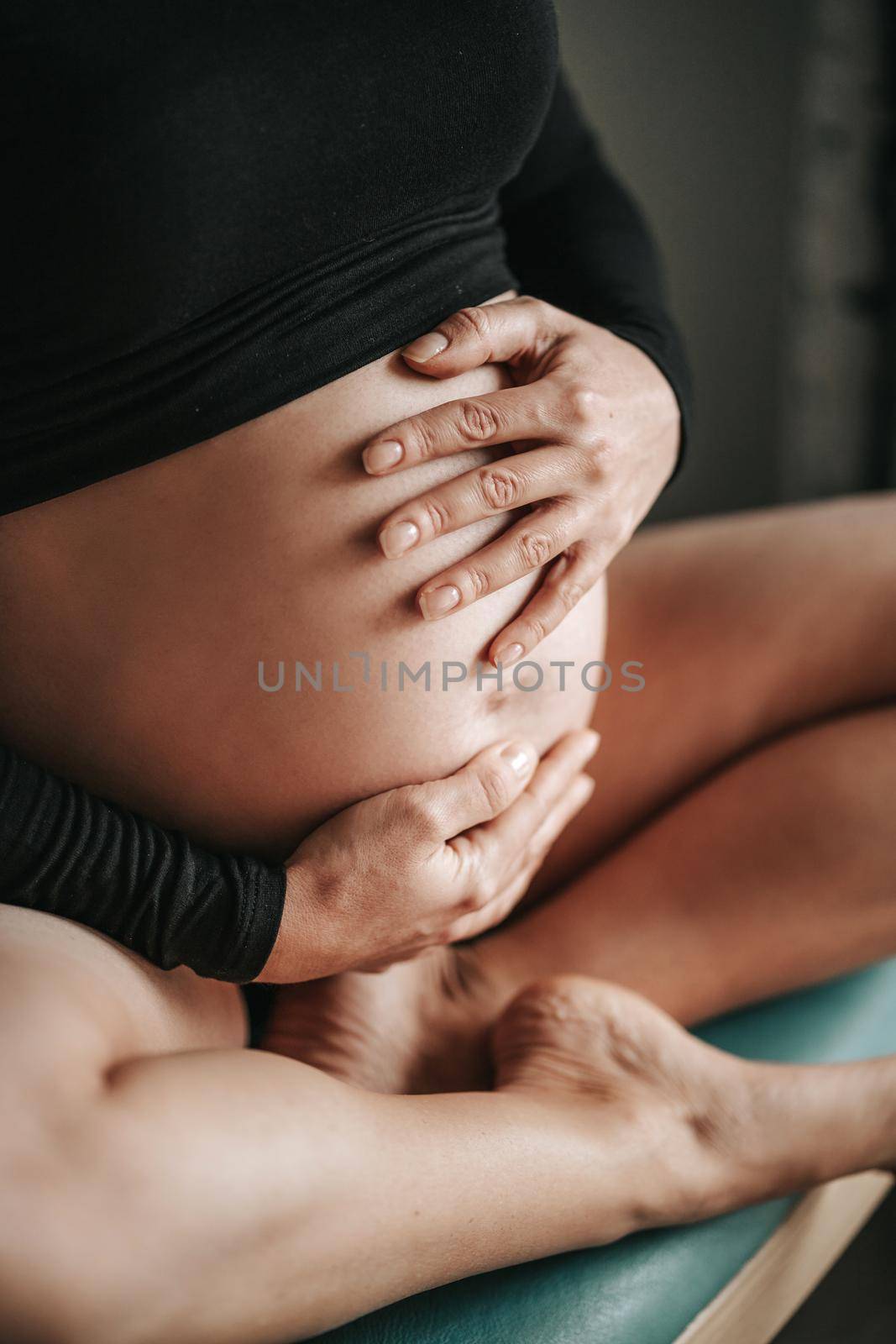 Pregnant woman sitting in black knee-high, holding her belly with her hands. High quality photo