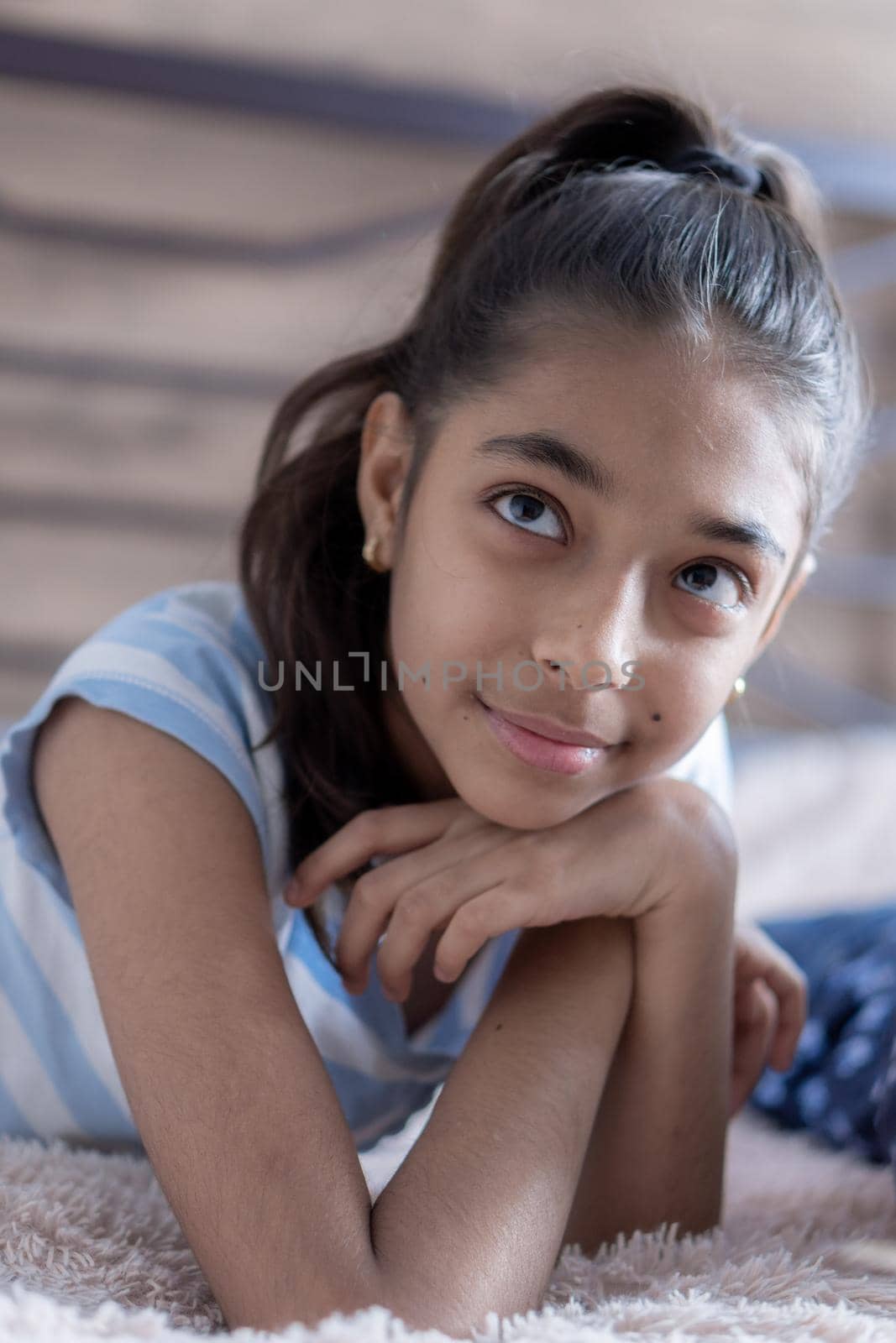 Closeup portrait of a young swarthy girl on a bed in the sun. Persian black-haired girl cute looks lying on the bed holding a smartphone