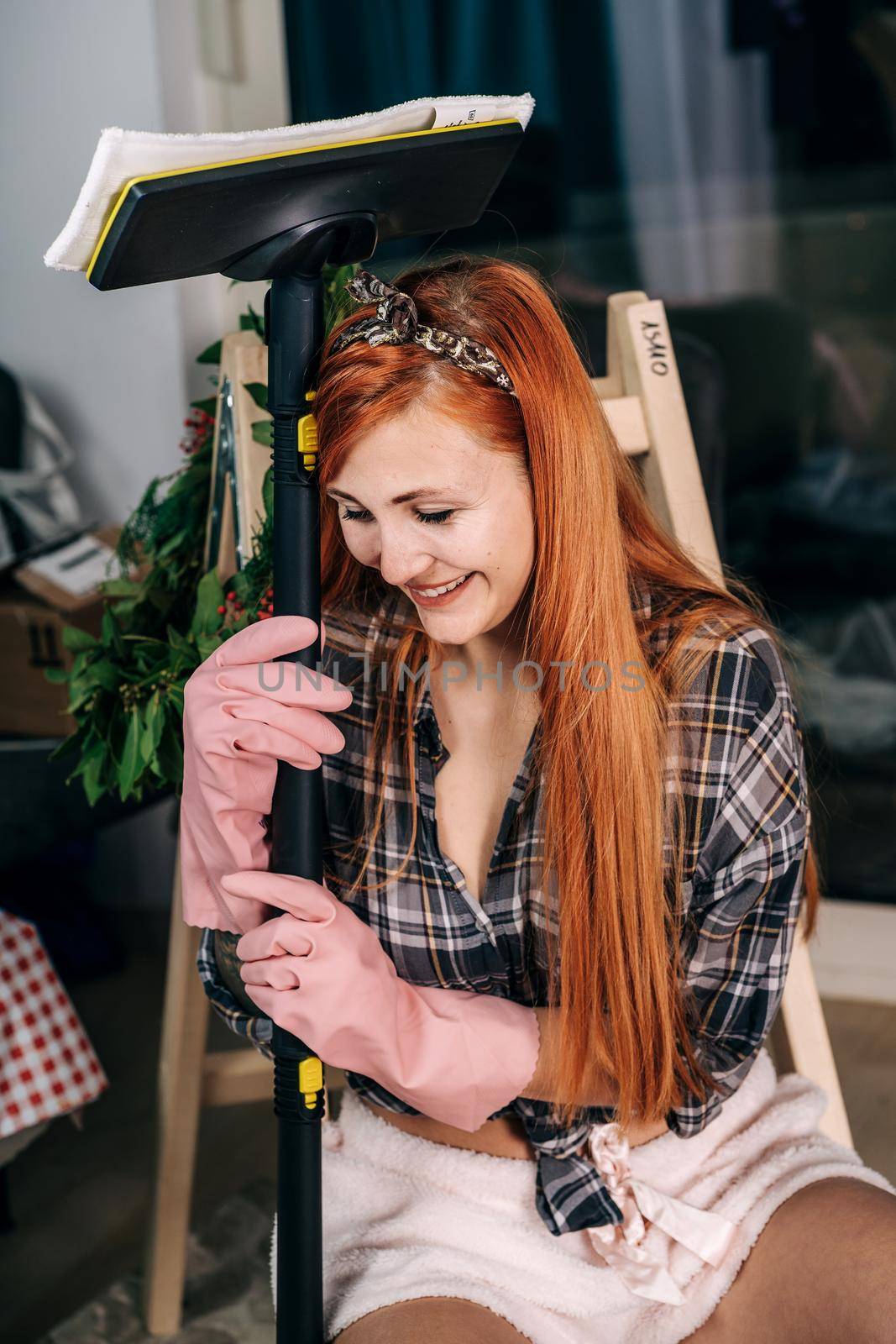 A young housewife in rubber gloves and a shirt holds a vacuum cleaner in her hands. Tired girl