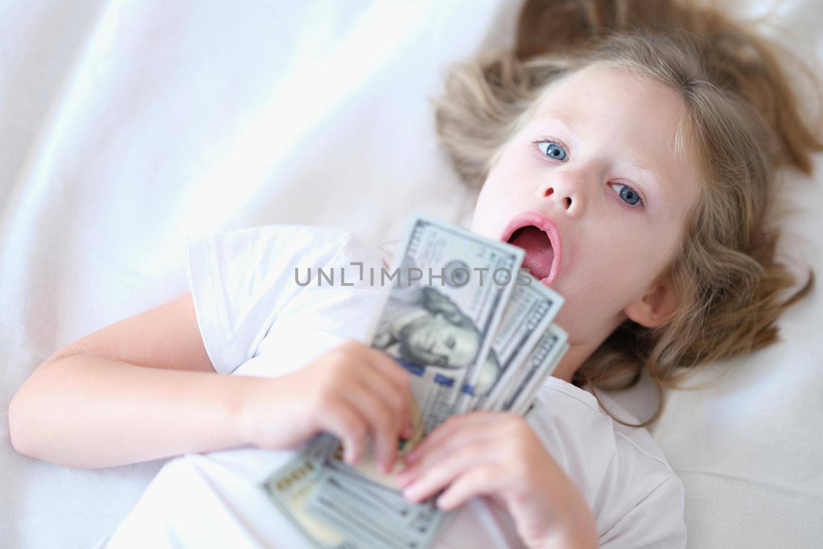 Portrait of small cheerful girl holding cash in hands. Little smiling child counting money, happy childhood.