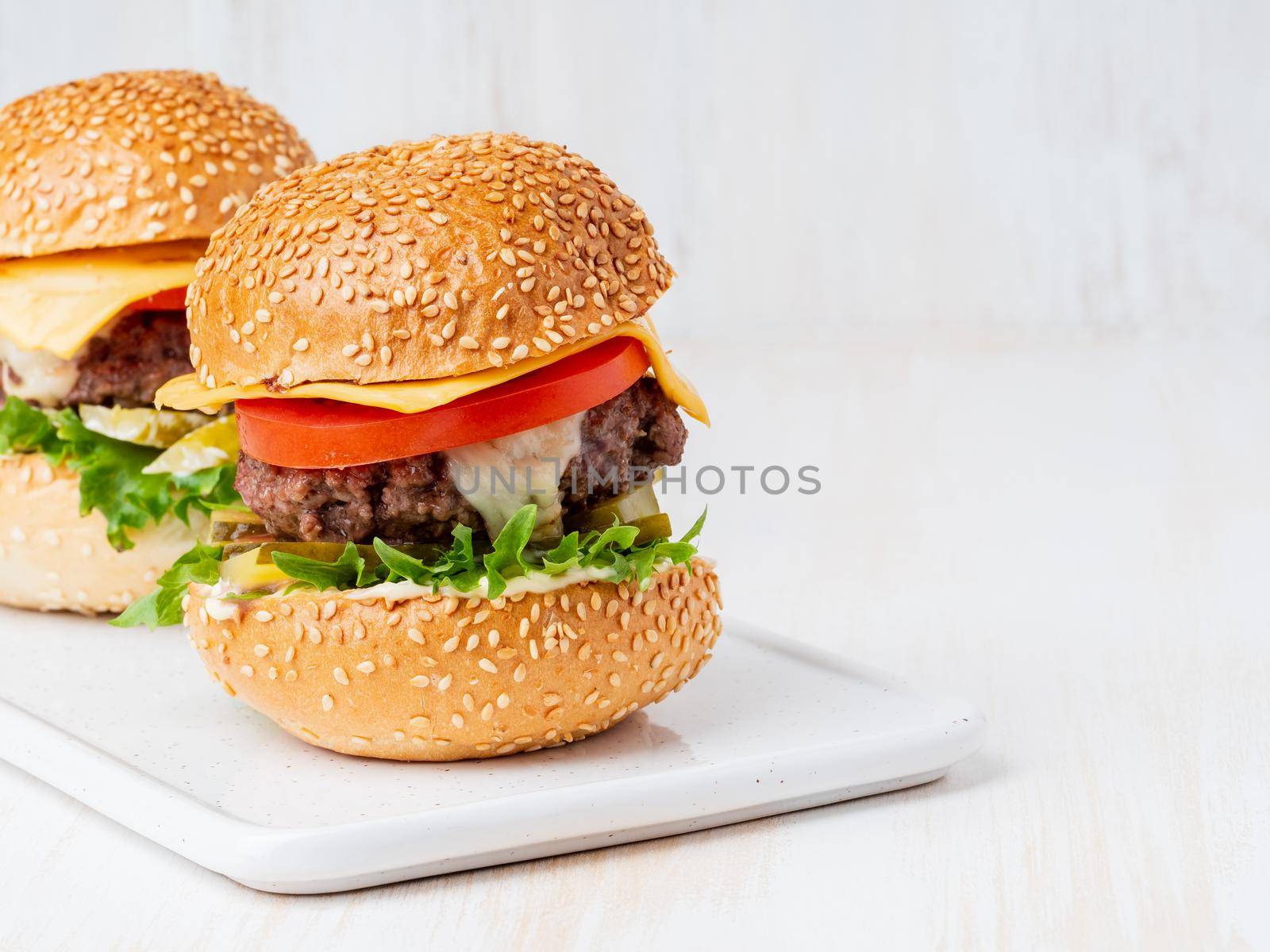 Two hamburgers on white board on white background, hot homemade unhealthy fat food, copy space