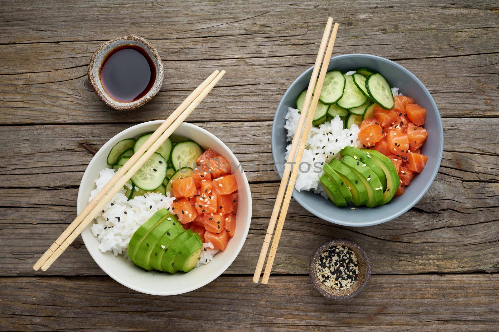 Salmon poke bowl with fresh fish, rice, cucumber, avocado with black and white sesame. Old wooden table. Food concept.
