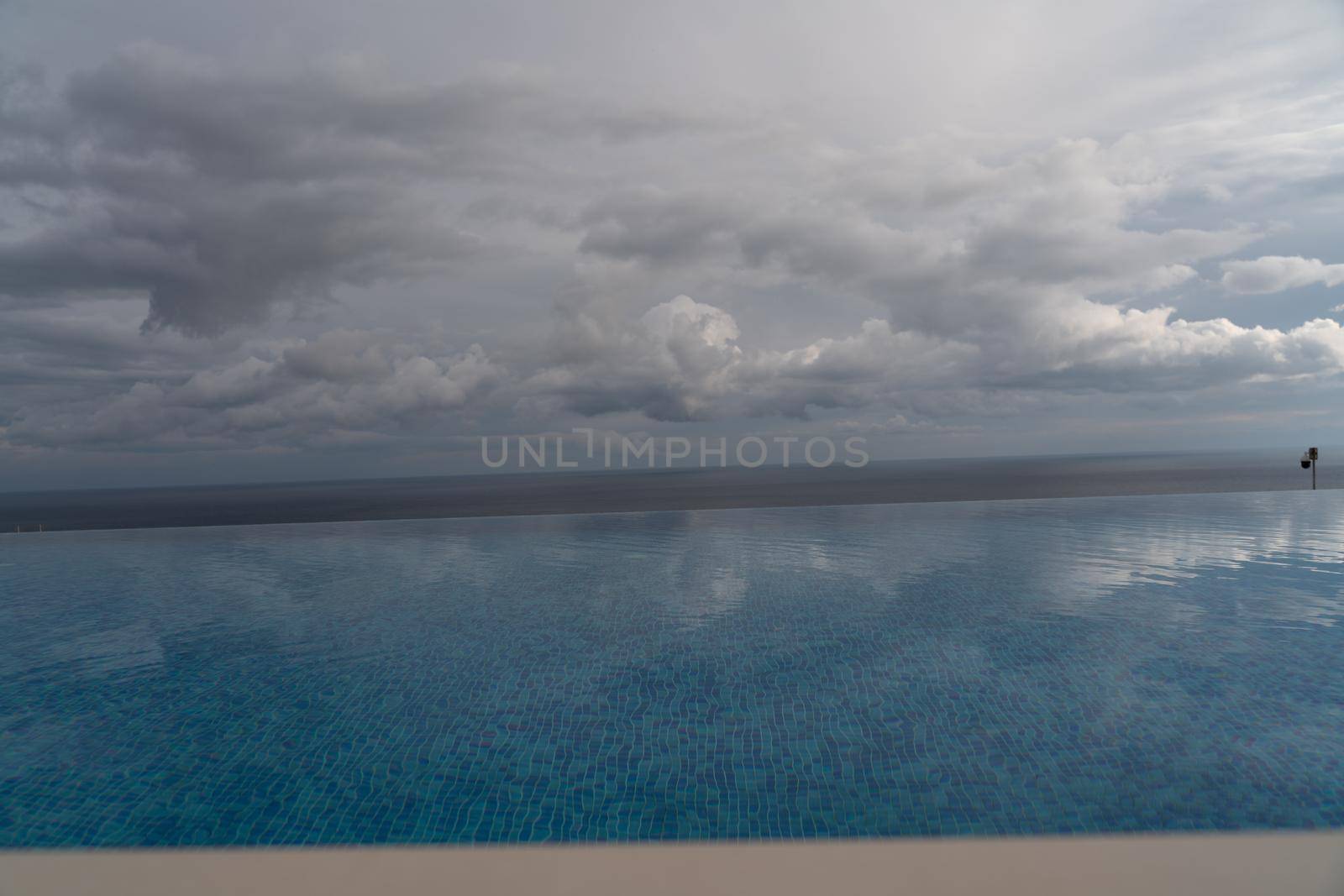 Infinity pool with sea and ocean views on the background of the sky with clouds. The clouds are reflected in the pool