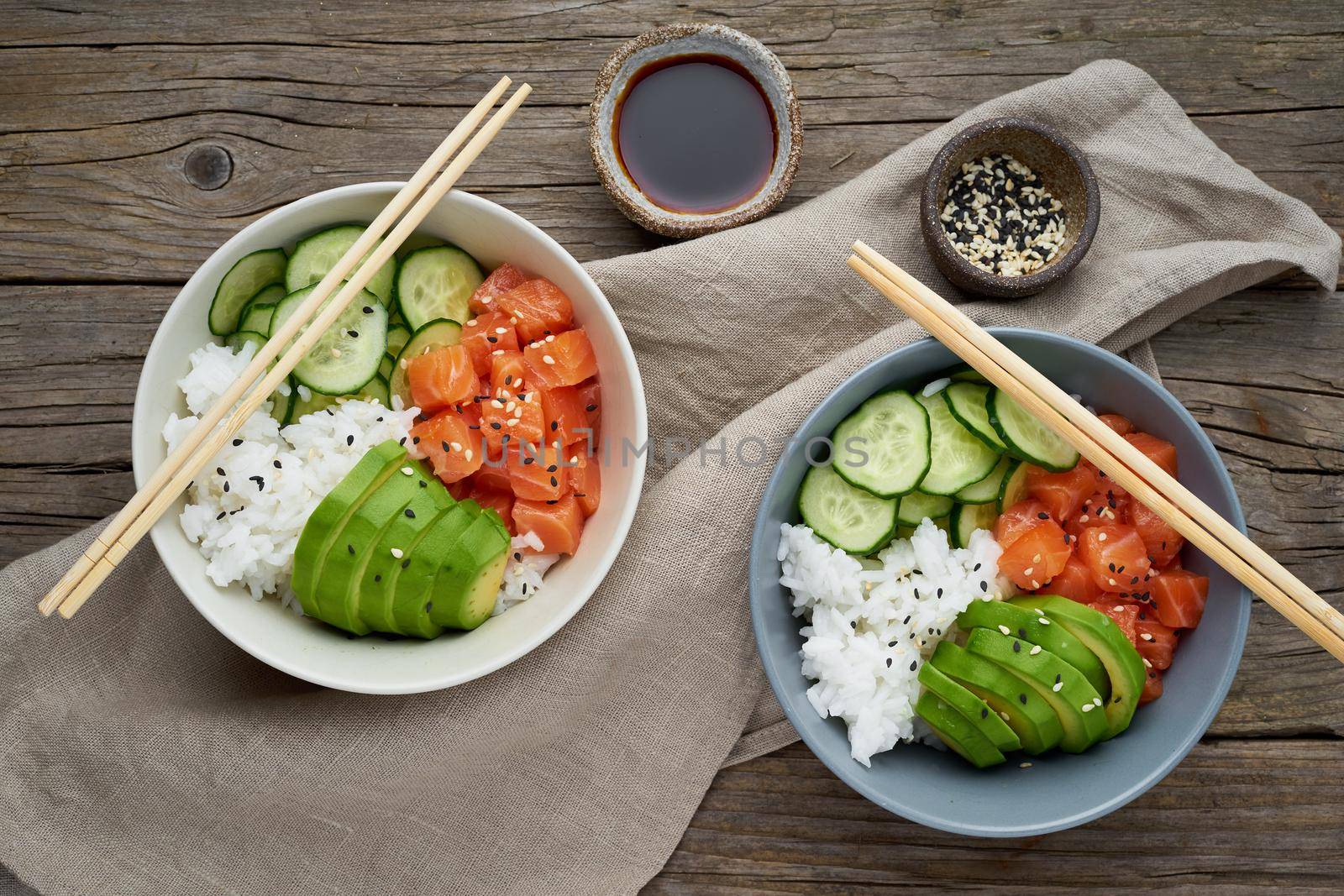 Salmon poke bowl with fresh fish, rice, cucumber, avocado with black and white sesame. Old wooden table. Food concept.
