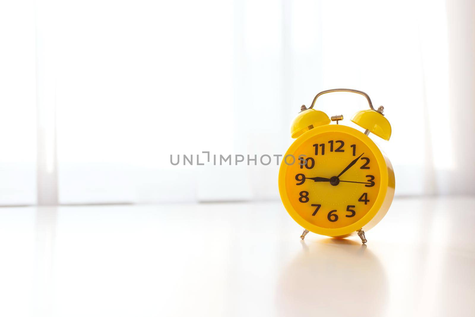 on a white table near the window with white curtains, there is a yellow alarm clock. by Zakharova