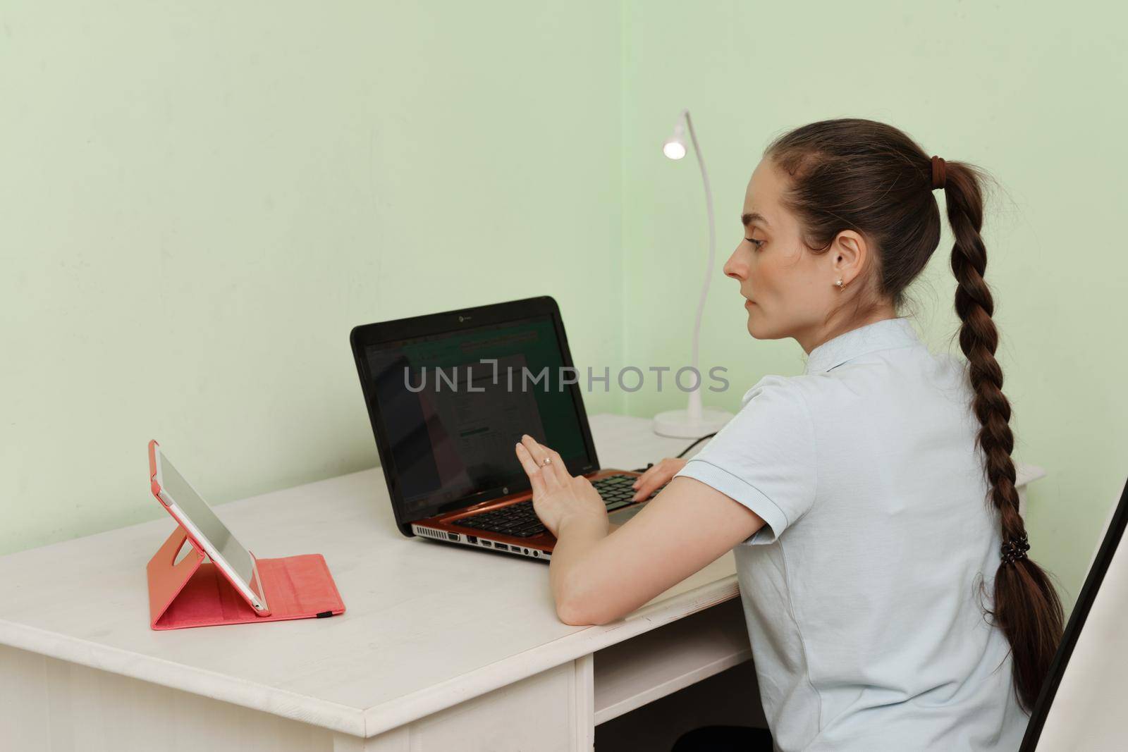 A young beautiful woman uses a laptop while sitting at her workplace, a cheerful smiling girl. Technology, business, homework, online learning, concept of learning, communication with loved ones quarantine distance education