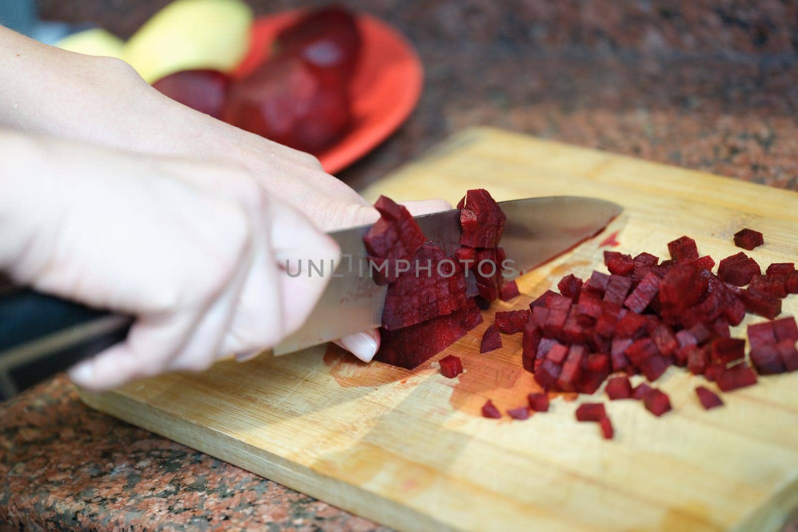Close-up of woman cutting red beet root, ingredients for dish. Beetroot cube slice. Female preparing dinner. Cooking concept