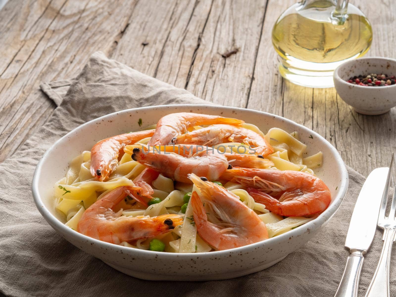 Shrimp, pasta tagliatelle, green peas, dill. White plate on old rustic wooden table, side view, copy space
