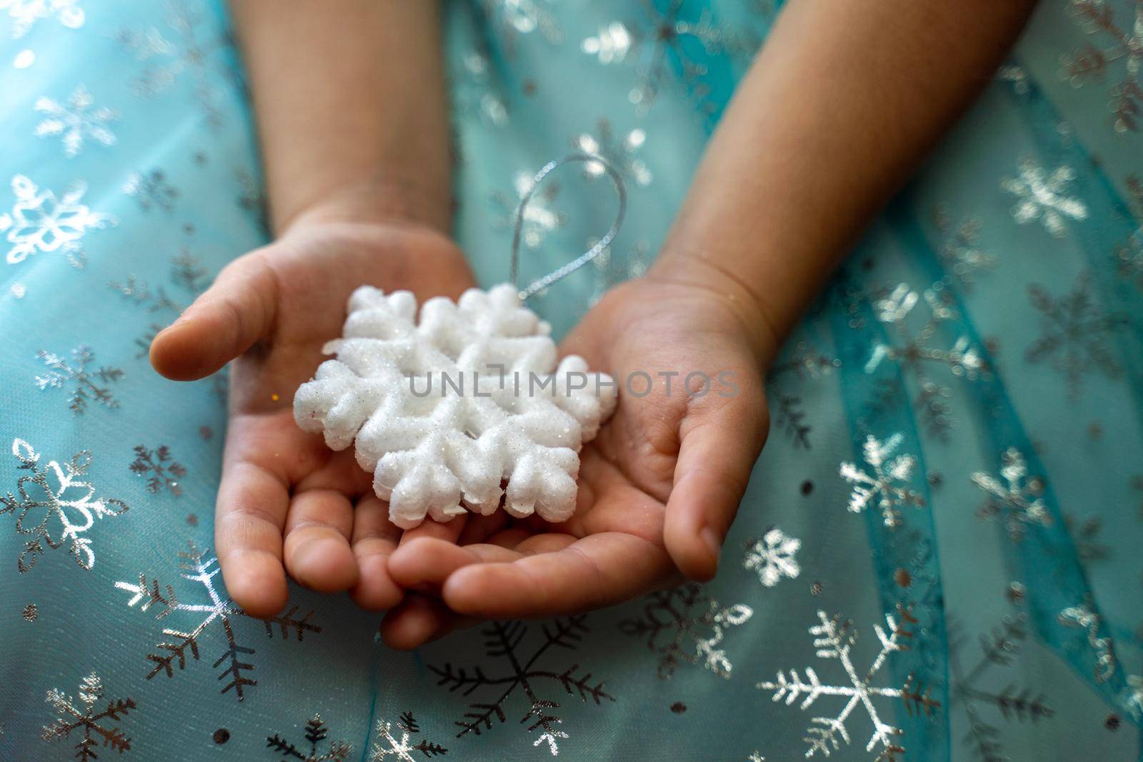 Winter and Christmas concept. Children's hands close-up holding a magic snowflake on the background of a blue dress with snowflakes. by Matiunina