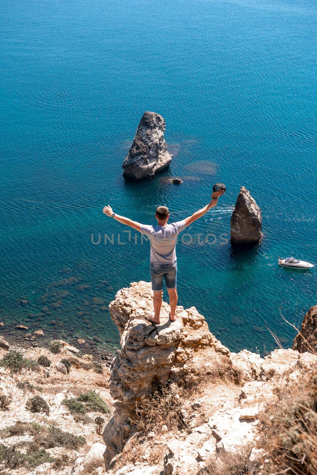 A male traveler in shorts and a T-shirt, facing the sea, raised his hands in the air. The concept of tourism and travel around the world