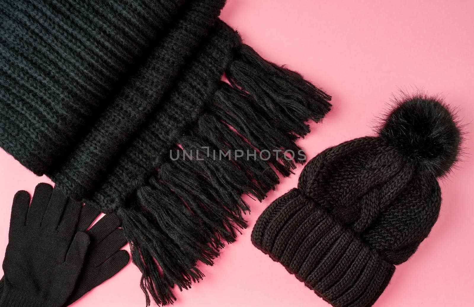 Flat lay winter or autumn warm woman accessories - black knitted scarf, hat, bag on bright pink background, copy space.