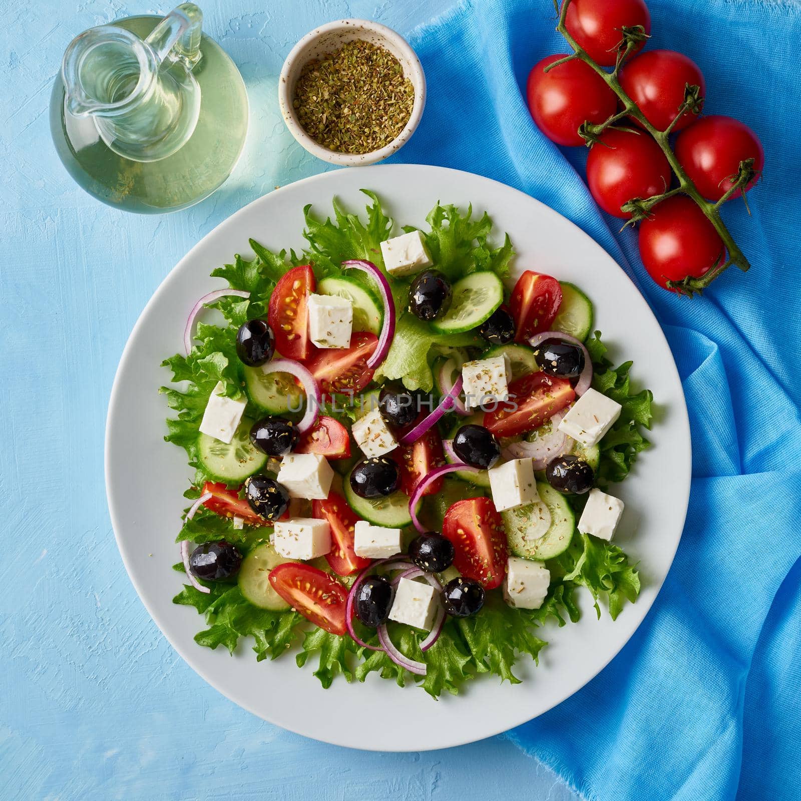 Greek salad on white plate on bright blue table, top view by NataBene