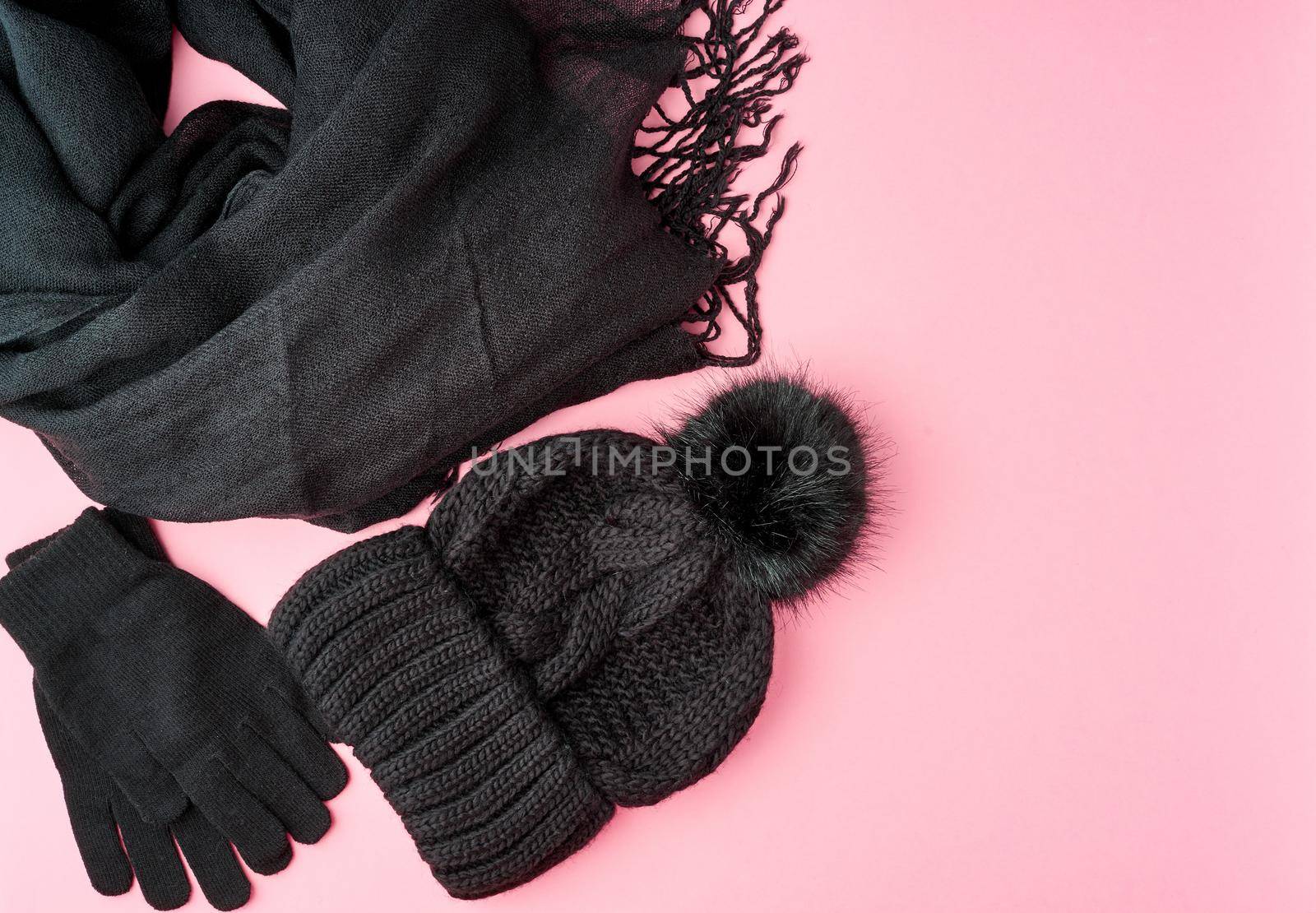 Flat lay winter or autumn warm woman accessories - black knitted scarf, hat on bright pink background, copy space.