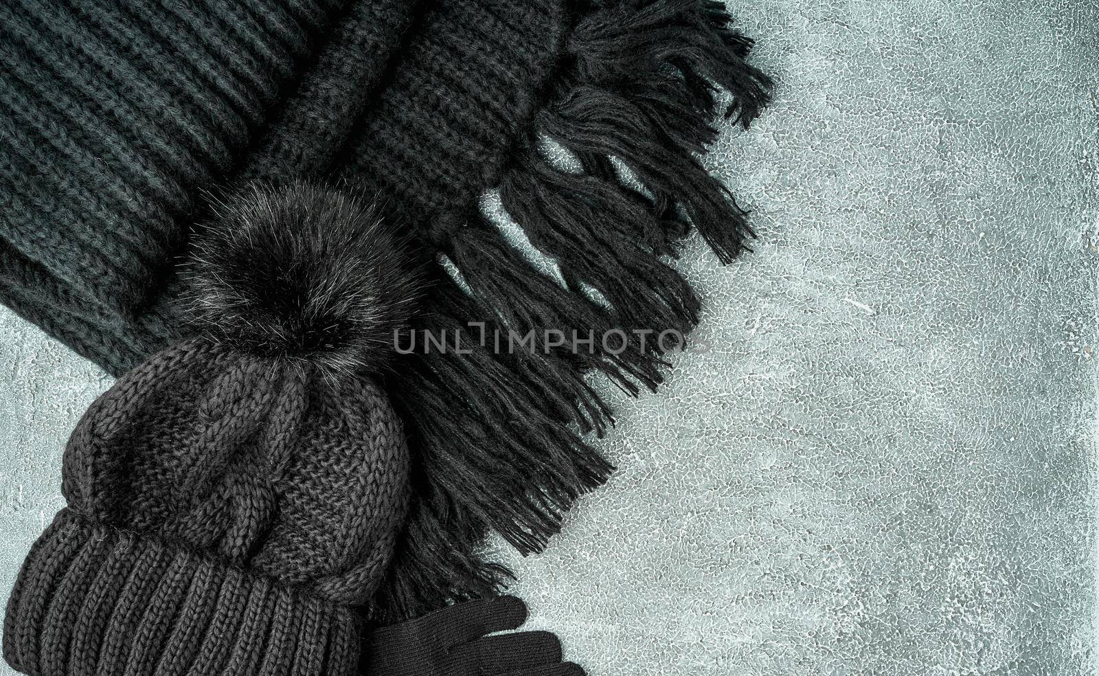 Flat lay winter or autumn warm woman accessories - black knitted scarf, hat on bright grey stone background, copy space.