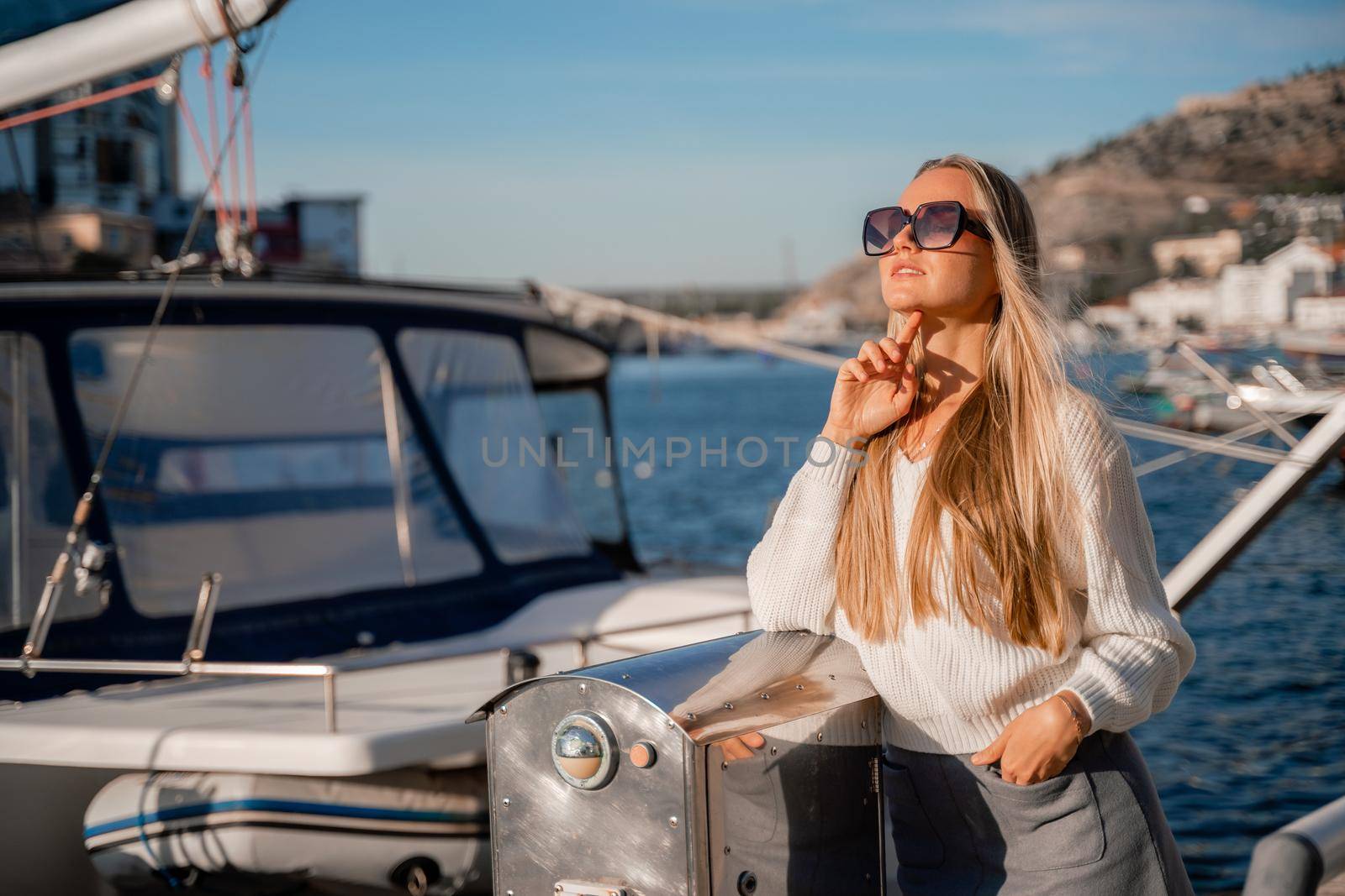 Outdoor photo of a romantic European blonde woman with long hair spending time outdoors exploring a European city. A graceful young lady enjoys the view of the embankment near the yacht.