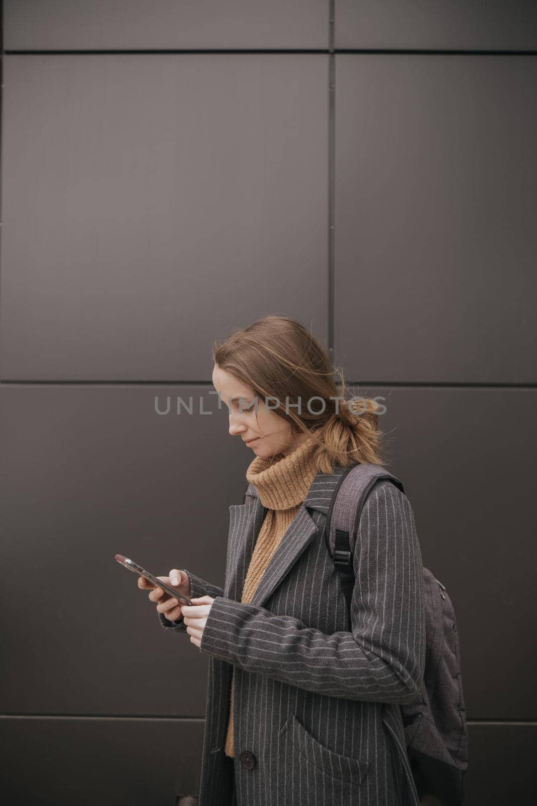 Portrait of happy hipster woman typing by mobile phone outdoors. Closeup cheerful girl walking with smartphone in urban background. Smiling lady holding cellphone in hands outside. by Symonenko